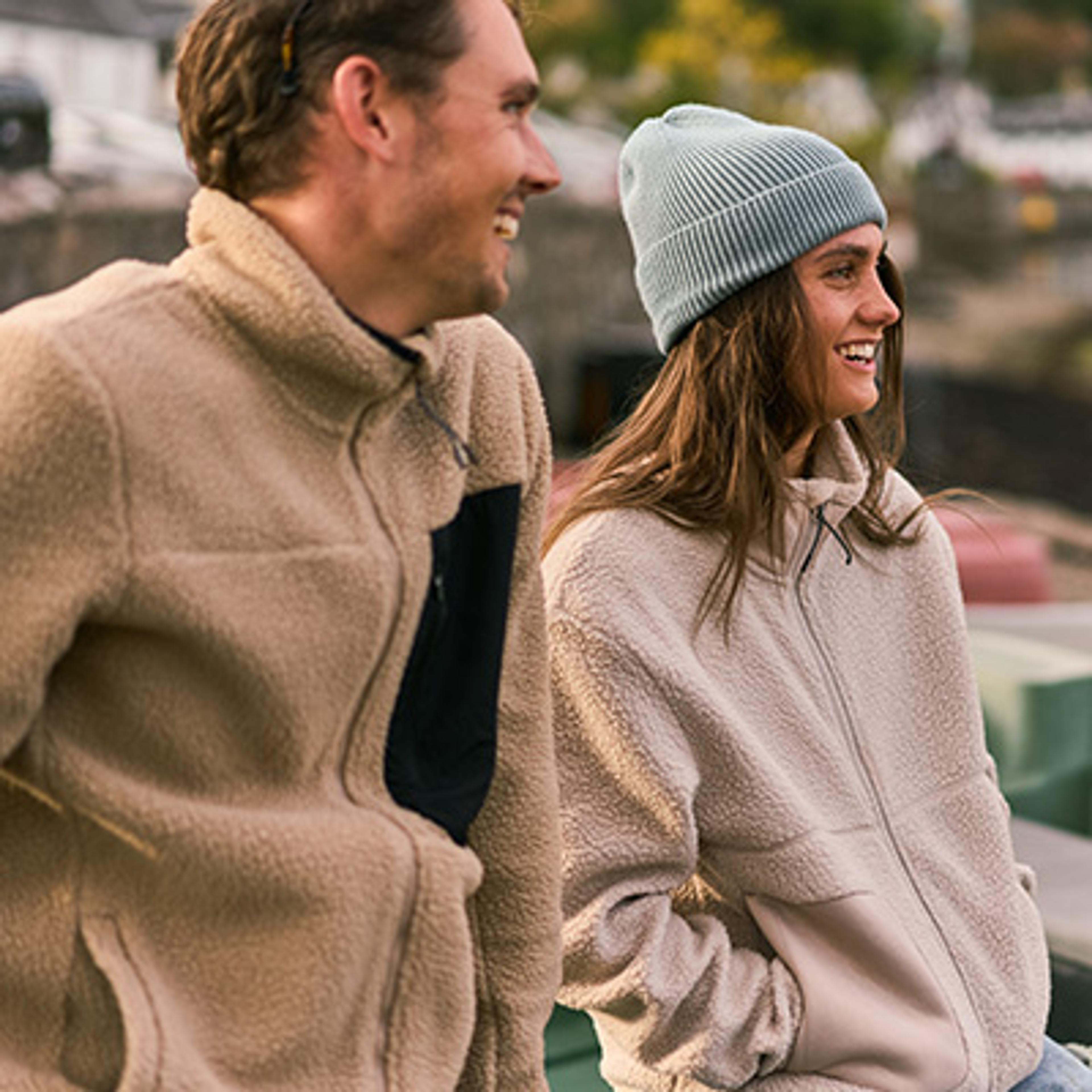 a man and a woman are standing next to each other and smiling . the woman is wearing a beanie .