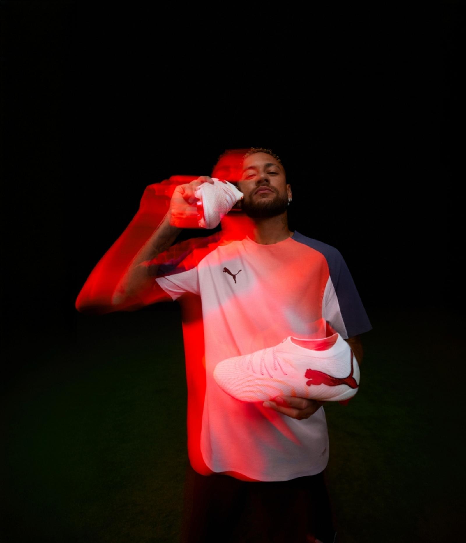 Neymar Jr. holding a white and red Puma football boot, with a red light streak and motion blur effect.