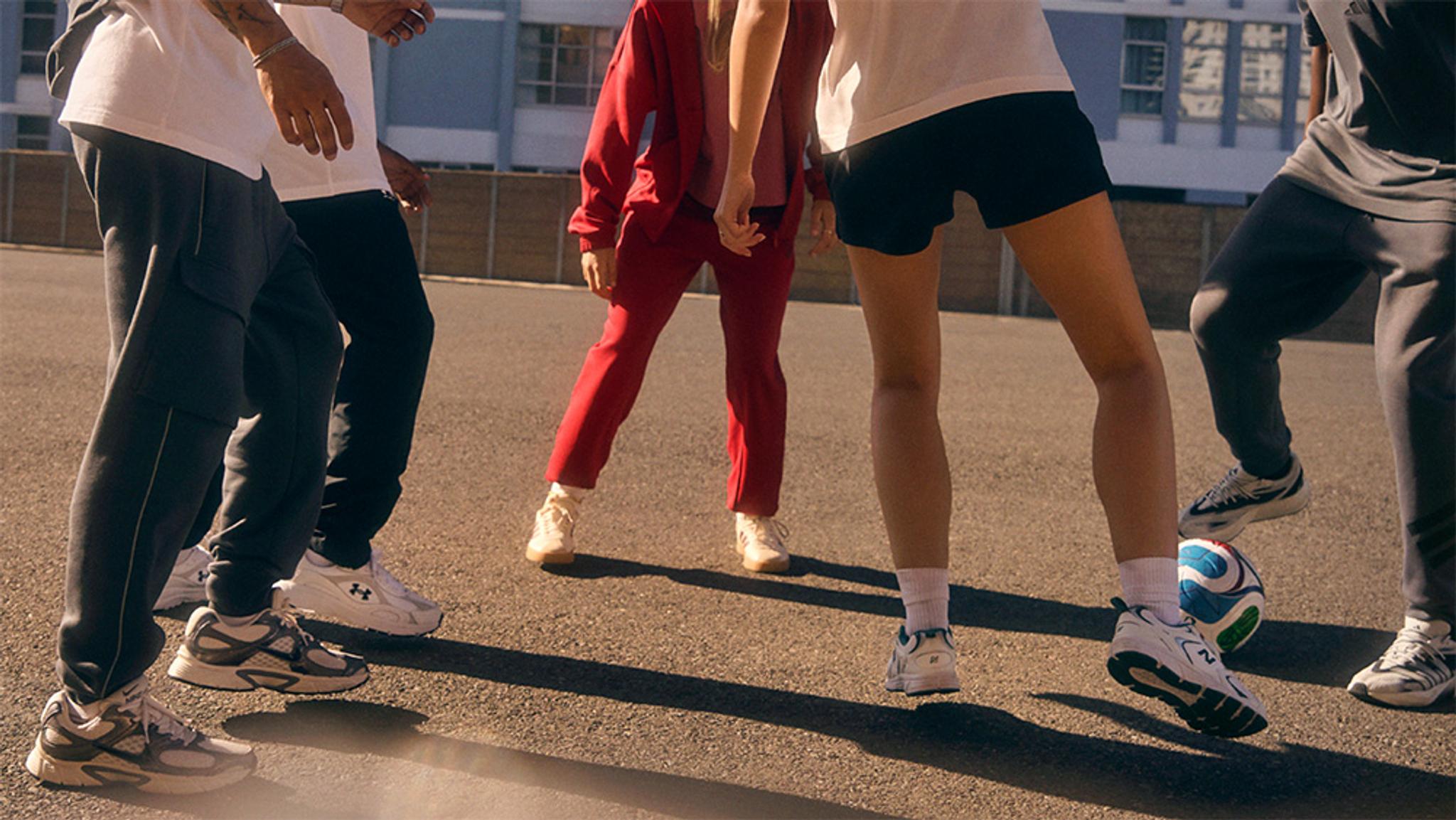 A group of people's legs and feet in athletic shoes, one foot on a soccer ball.