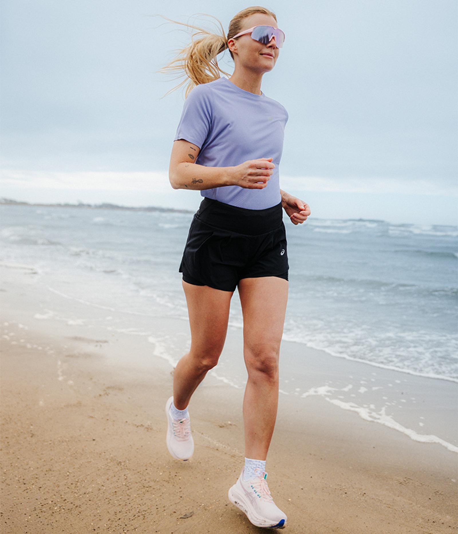 Woman in ASICS gear running on a paved path next to water. ASICS logo visible.
