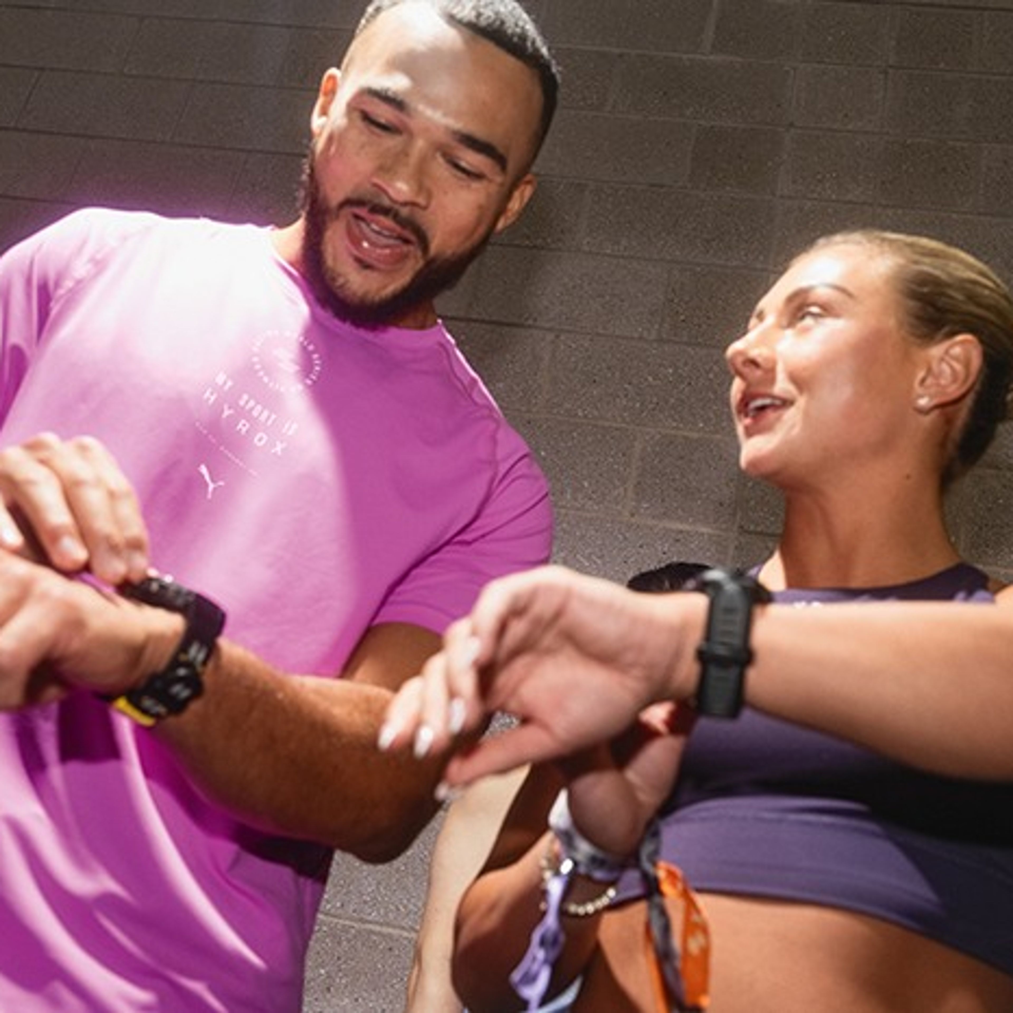 A man and woman in athletic wear looking at their smartwatches while talking.
