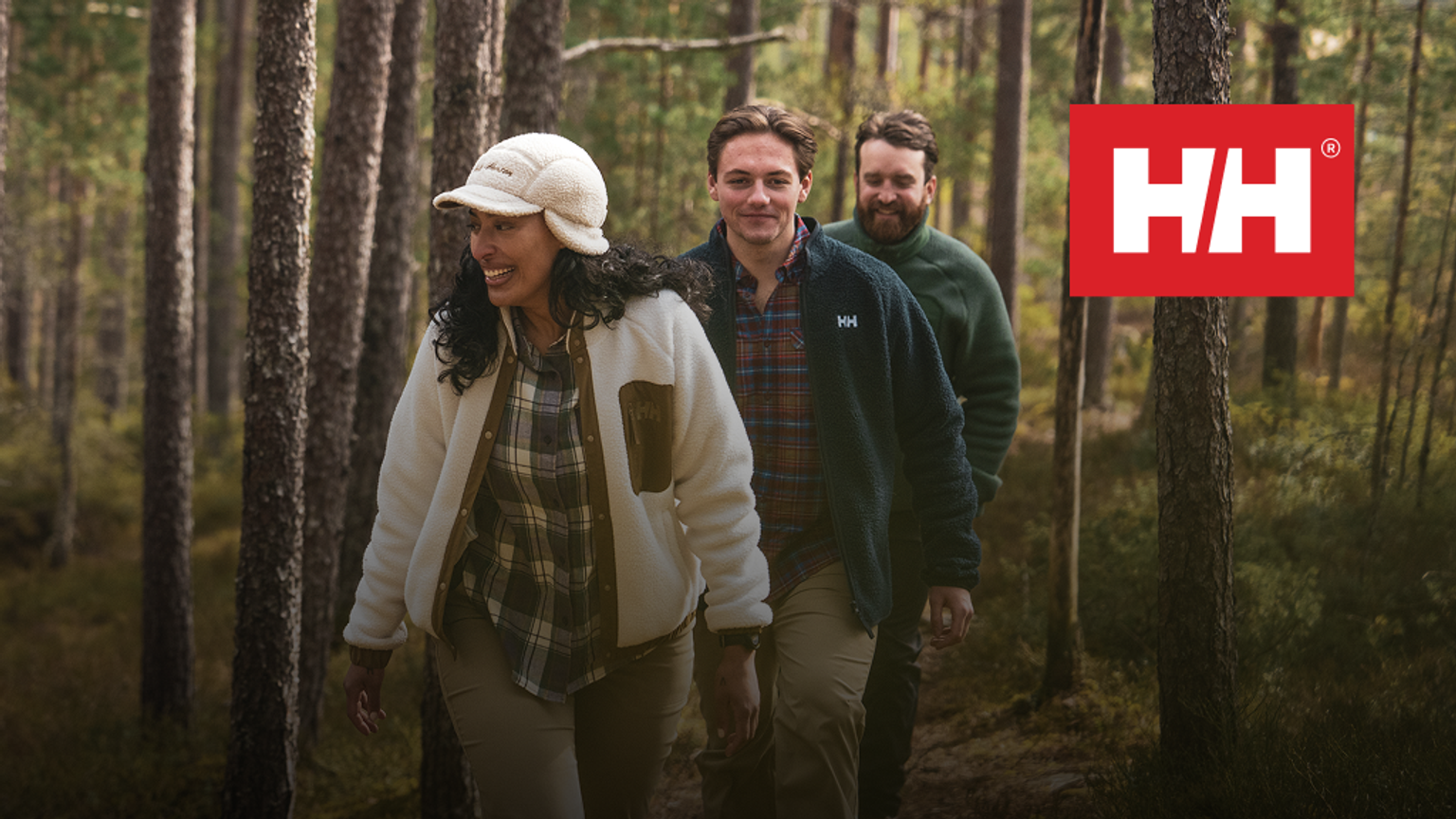 three people walking through a forest with a hh logo in the background