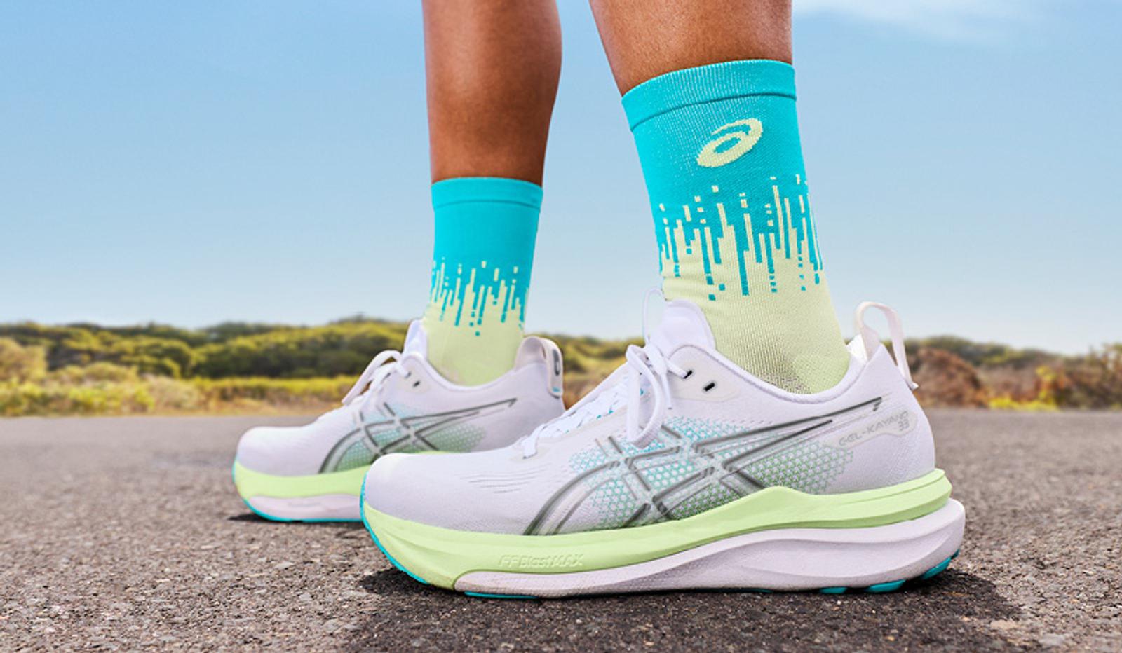 Close-up of a runner's feet in white and lime green ASICS shoes and matching gradient socks on a road.