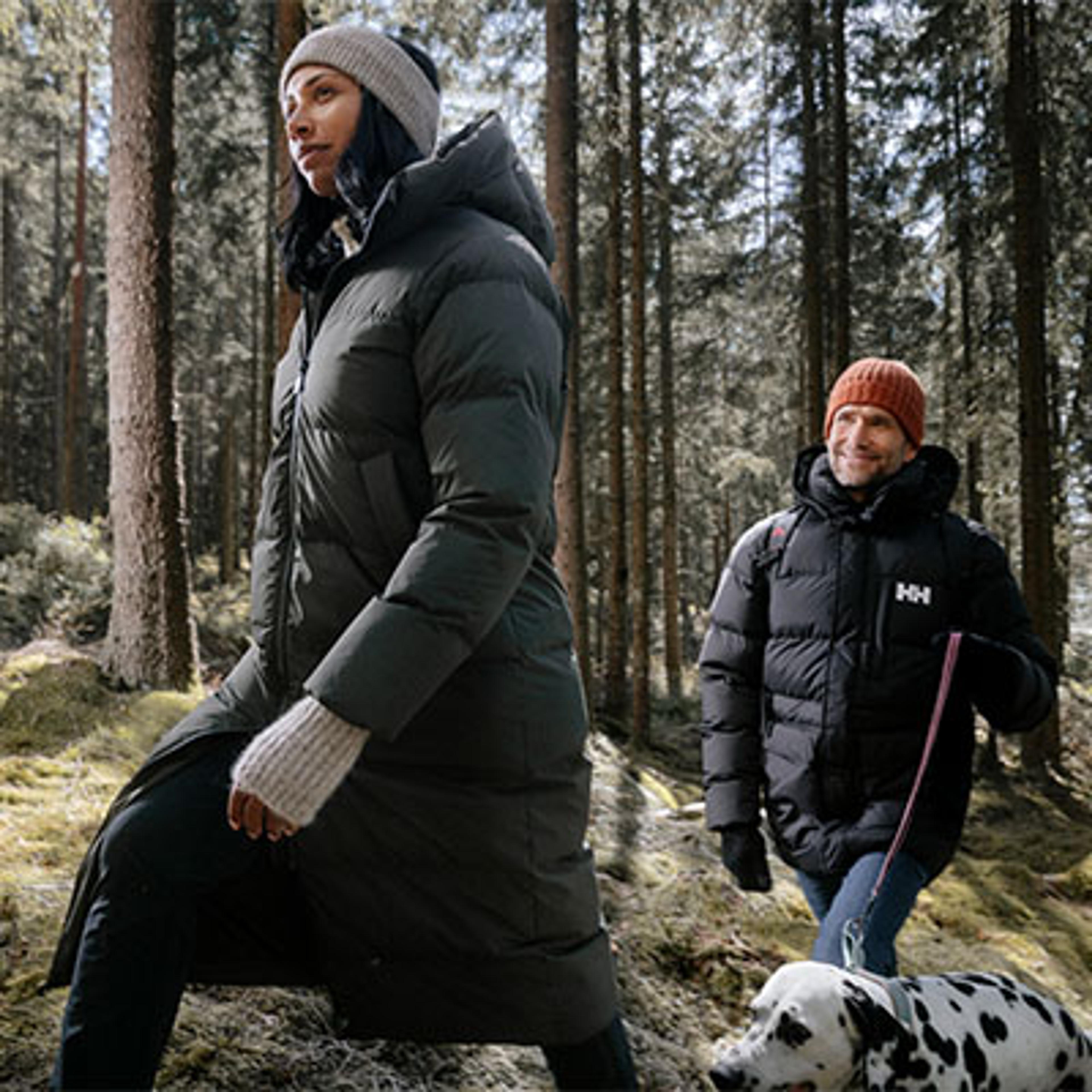a man and a woman are walking a dalmatian dog in the woods .