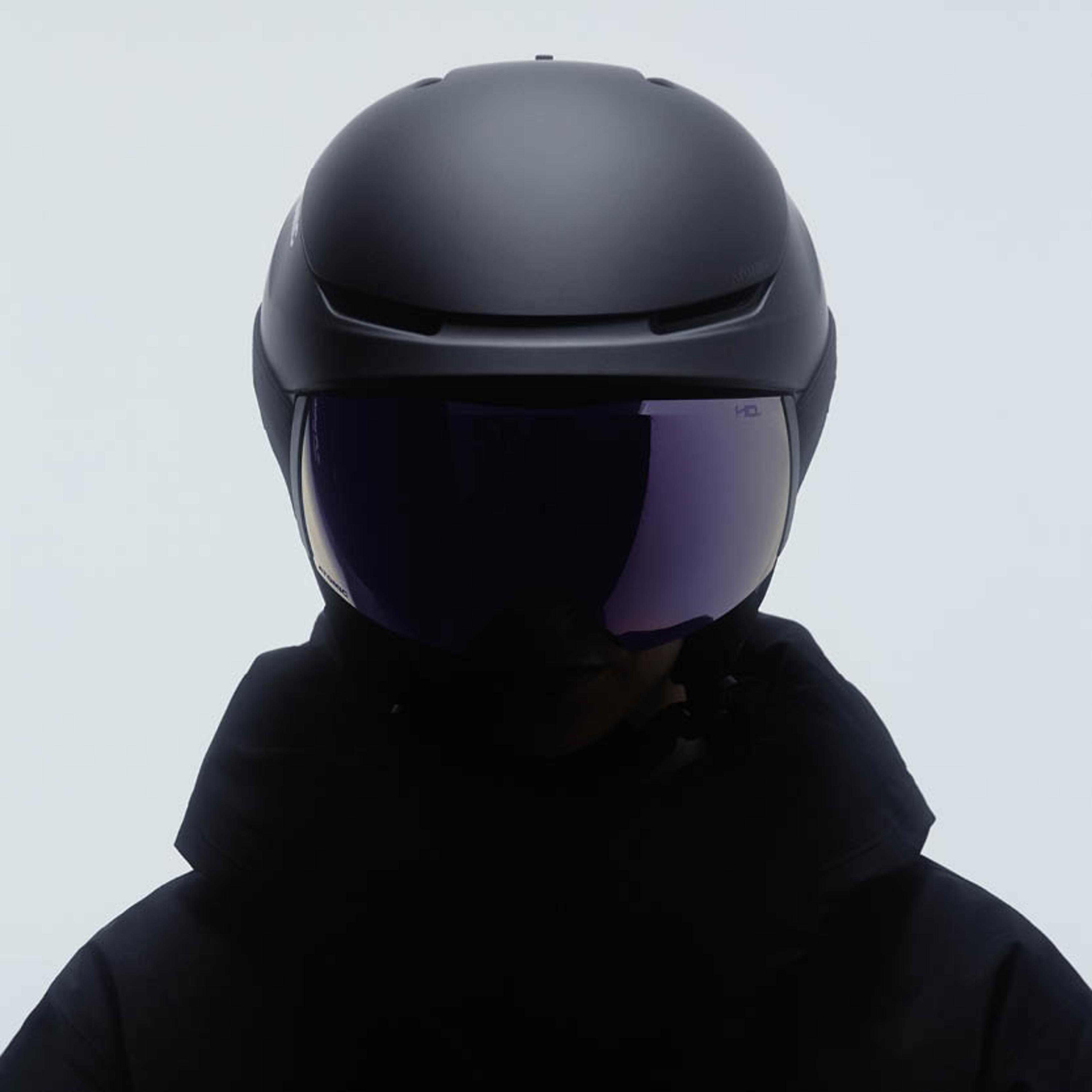 A person wearing a black ski helmet with a purple integrated visor.