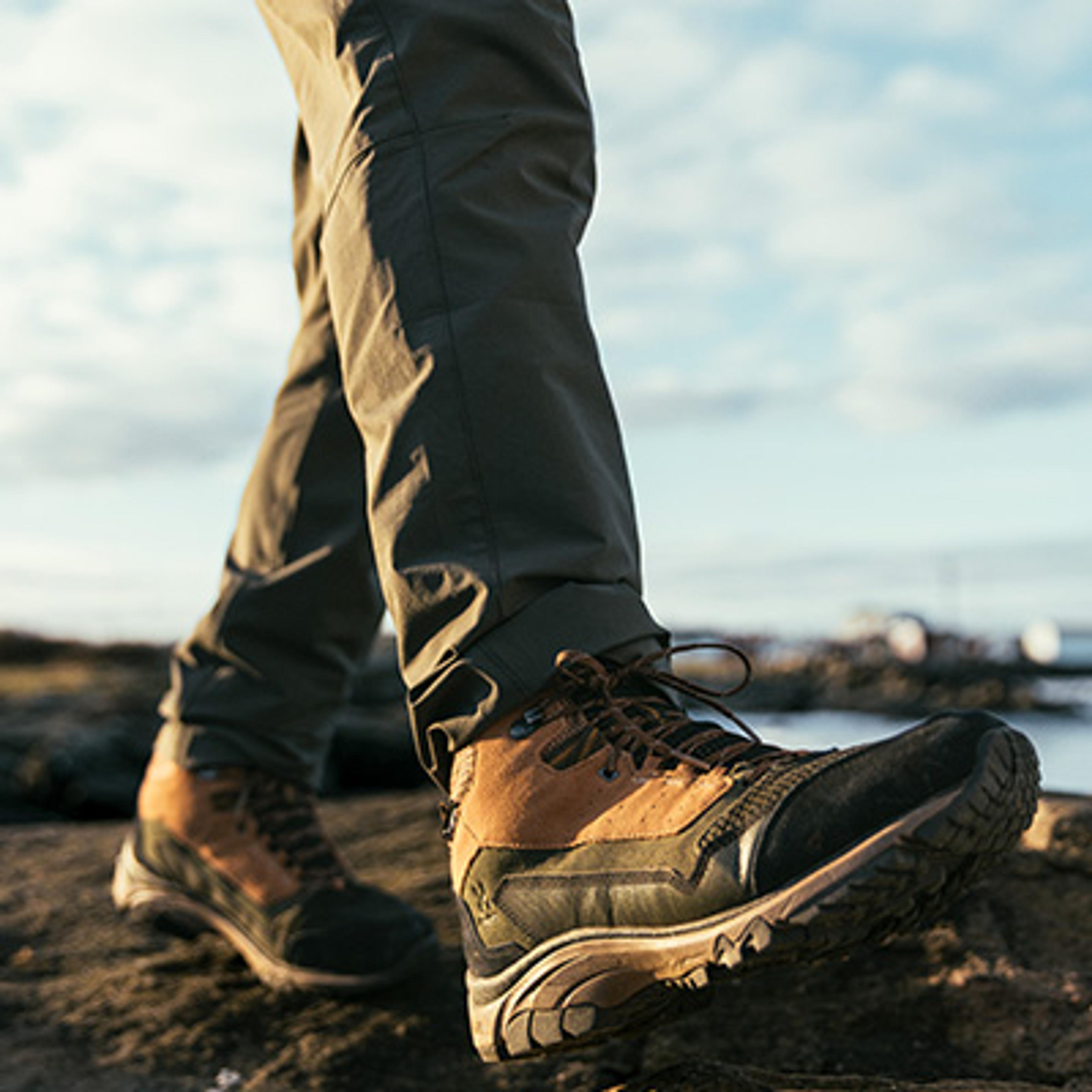 Person wearing hiking pants and multi-colored hiking boots walking on rocky ground.