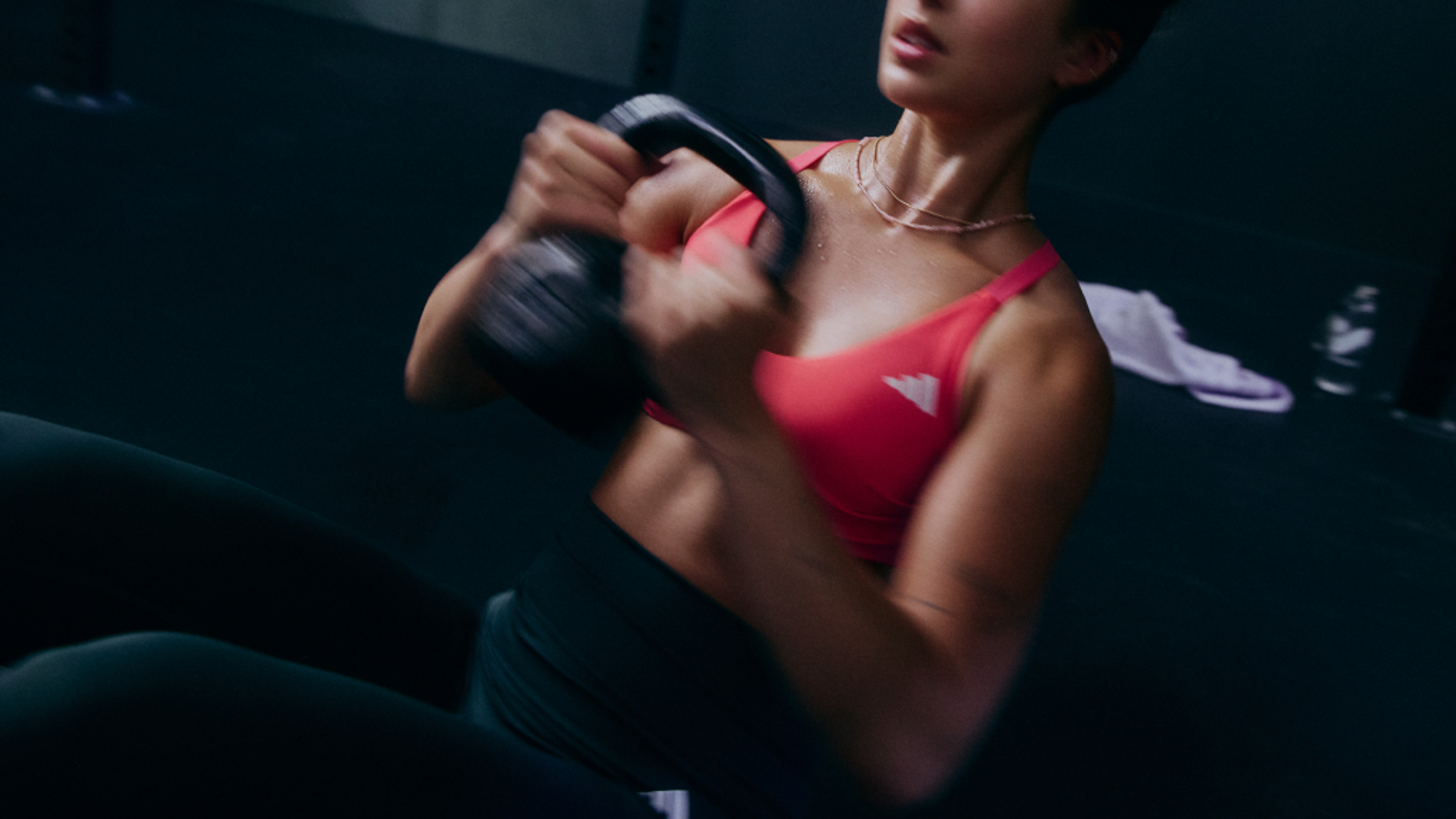 Sweaty woman in pink Adidas sports bra doing kettlebell swings, motion blurred.