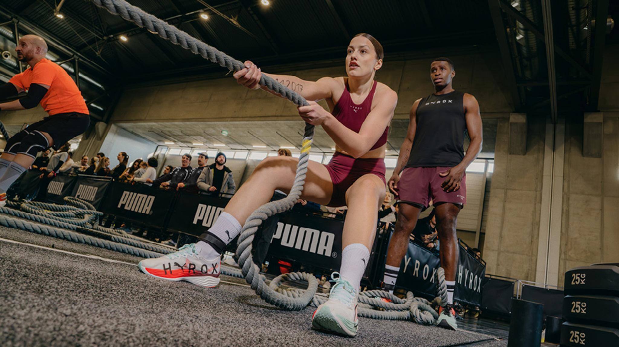 a woman is pulling a rope in a gym while a man watches .