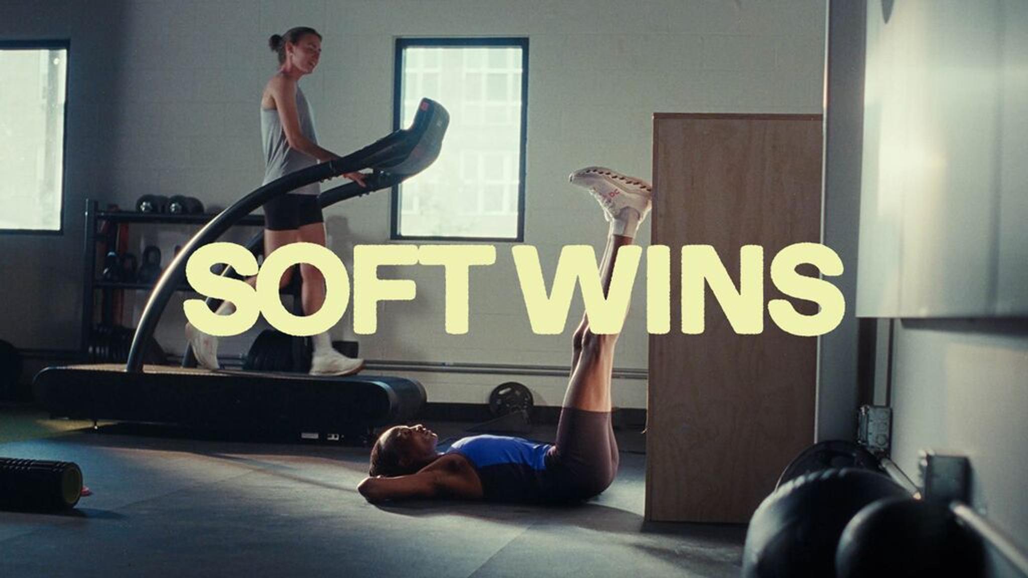 a woman is laying on the floor in a gym while another woman is running on a treadmill .