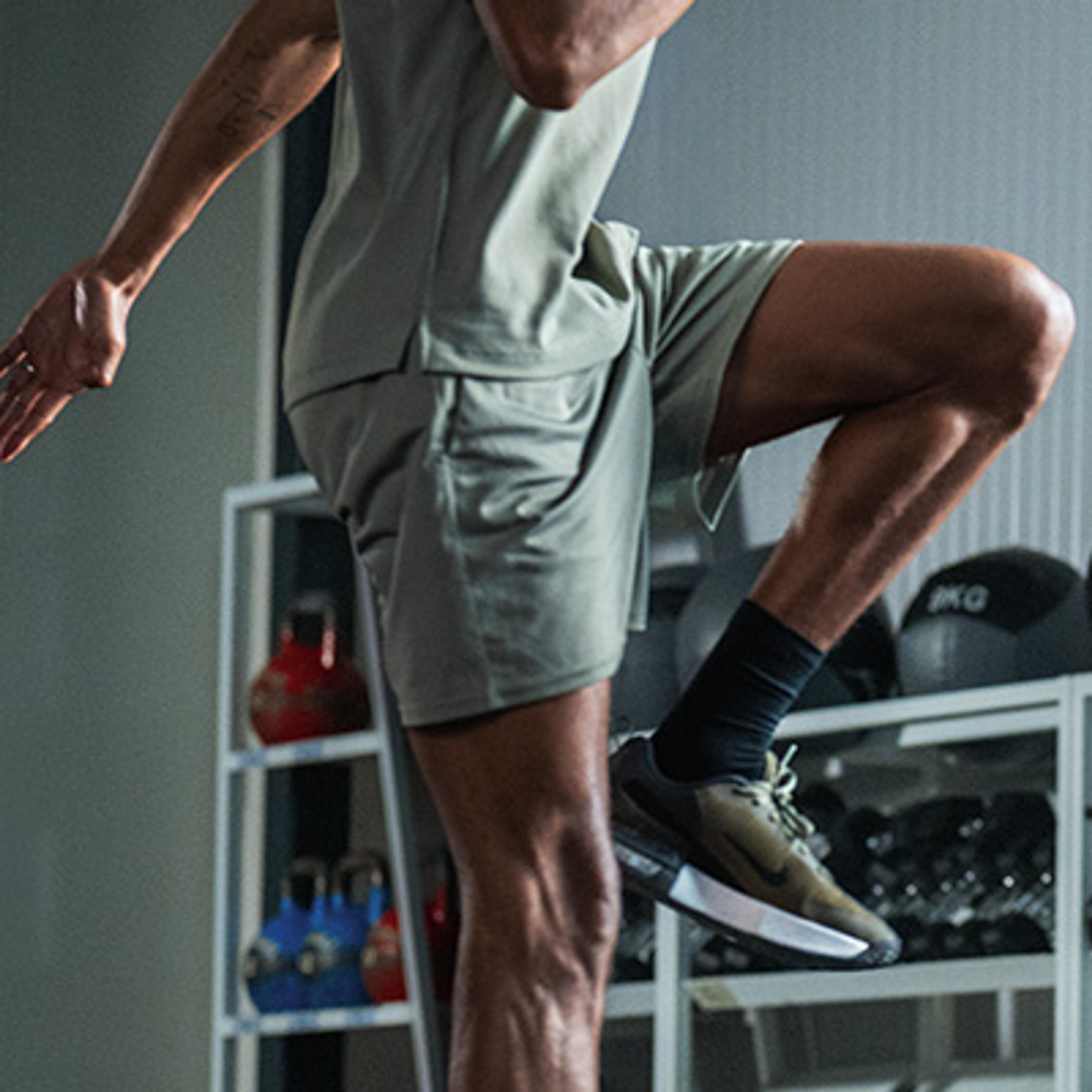 Person in athletic shorts and sneakers with one leg raised in a gym.