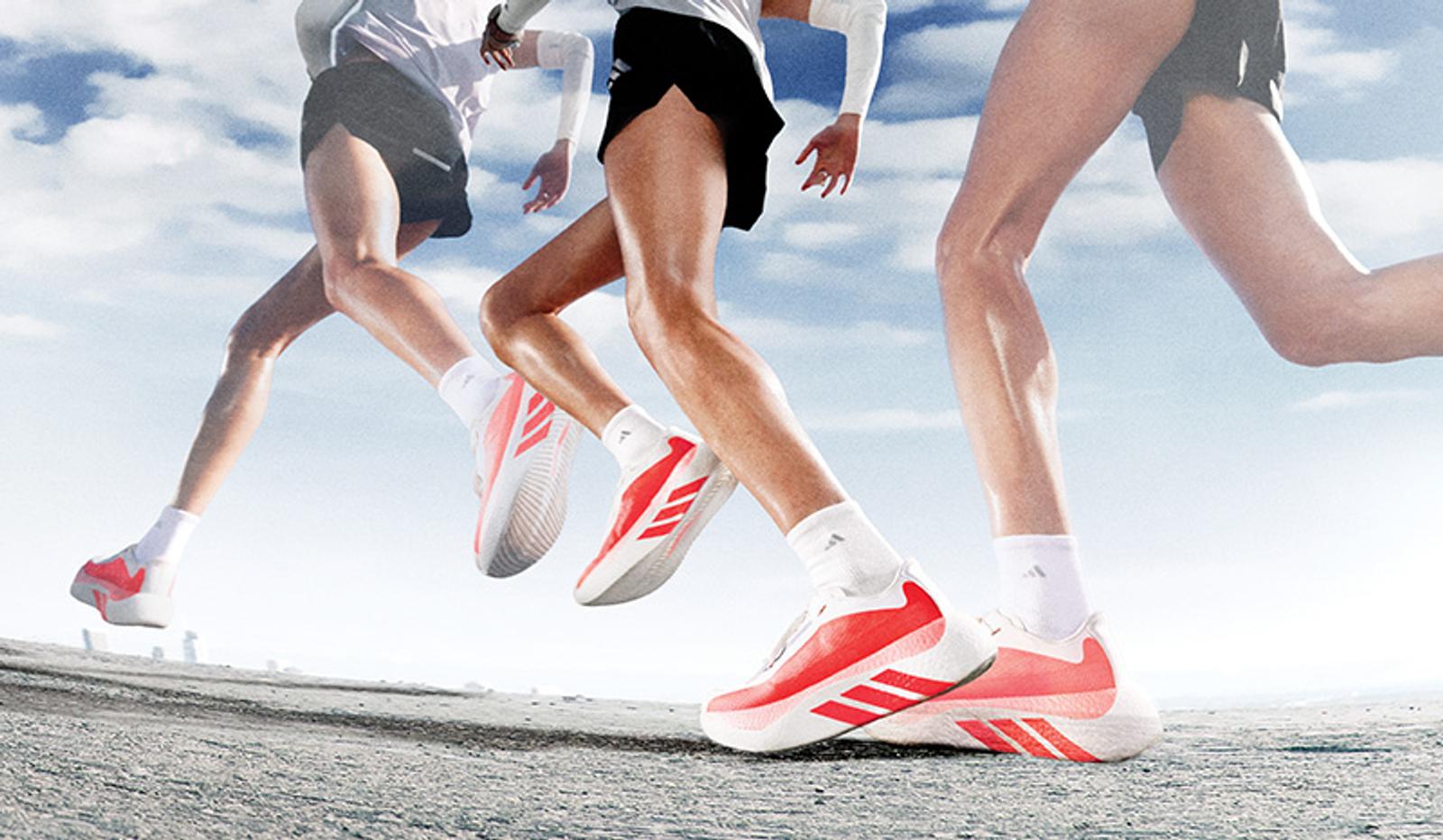 Three runners' legs in motion, wearing red and white athletic shoes on a road.