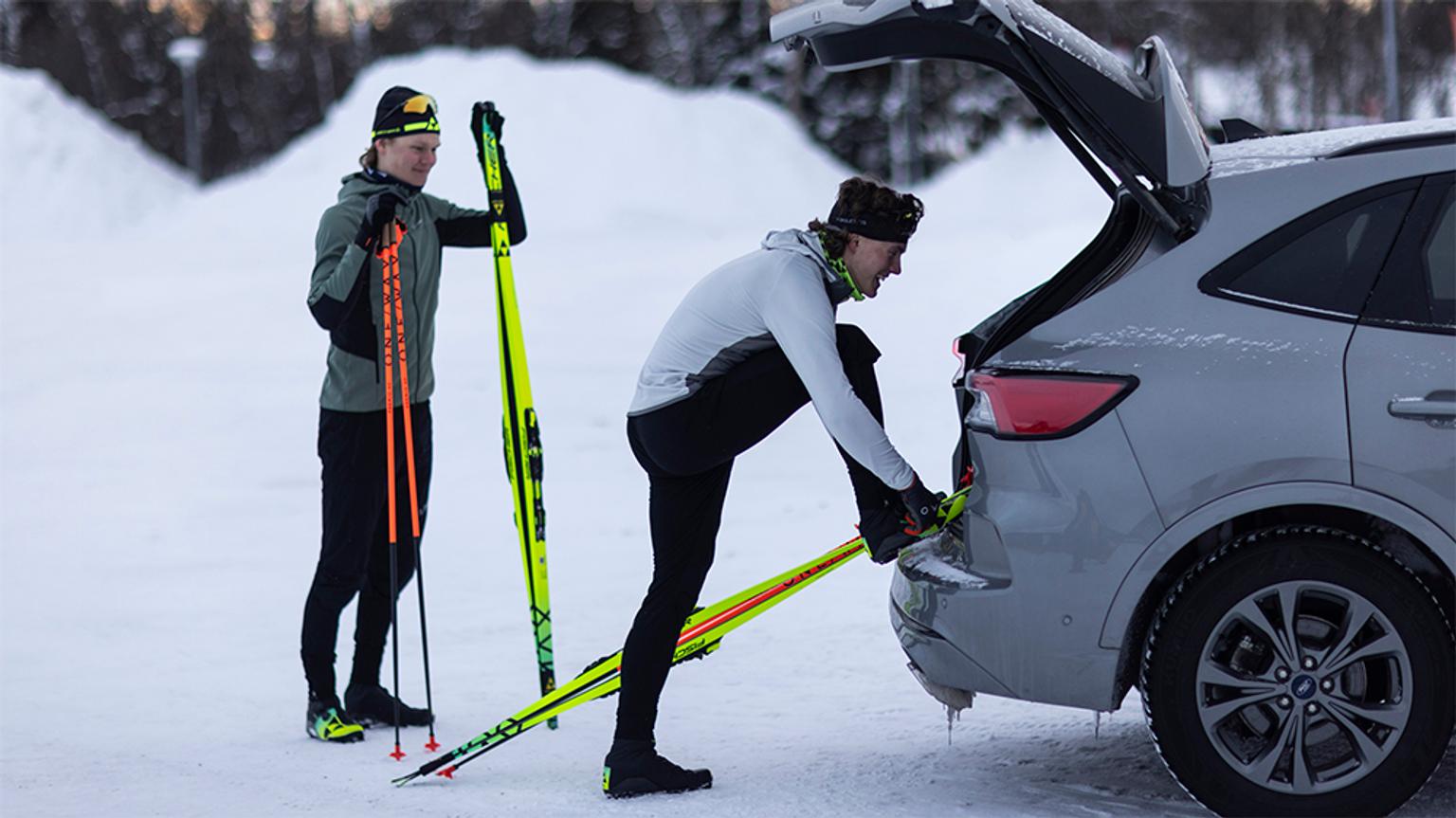 a man is putting skis in the back of a car .