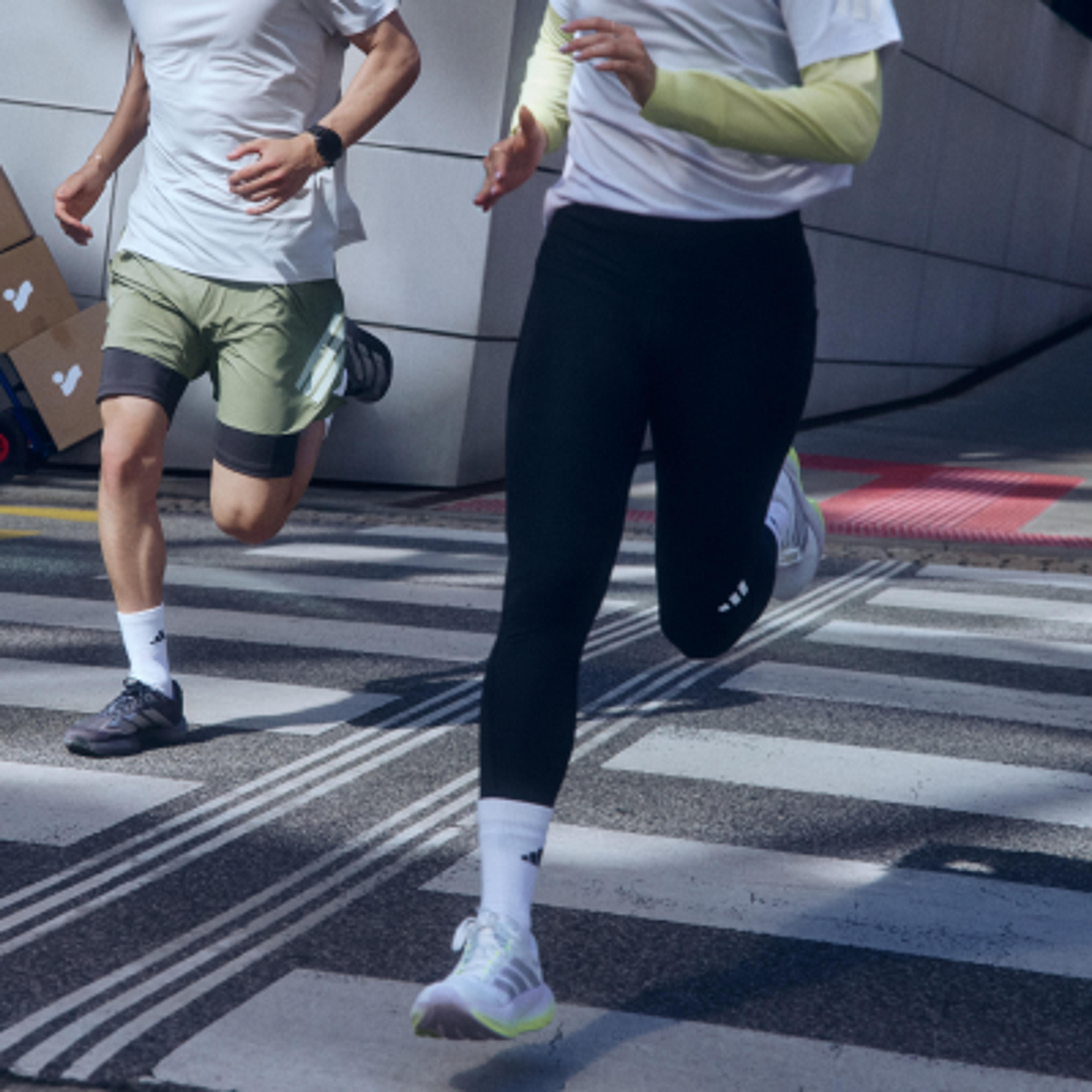 Two people running on a street crosswalk in Adidas athletic wear.