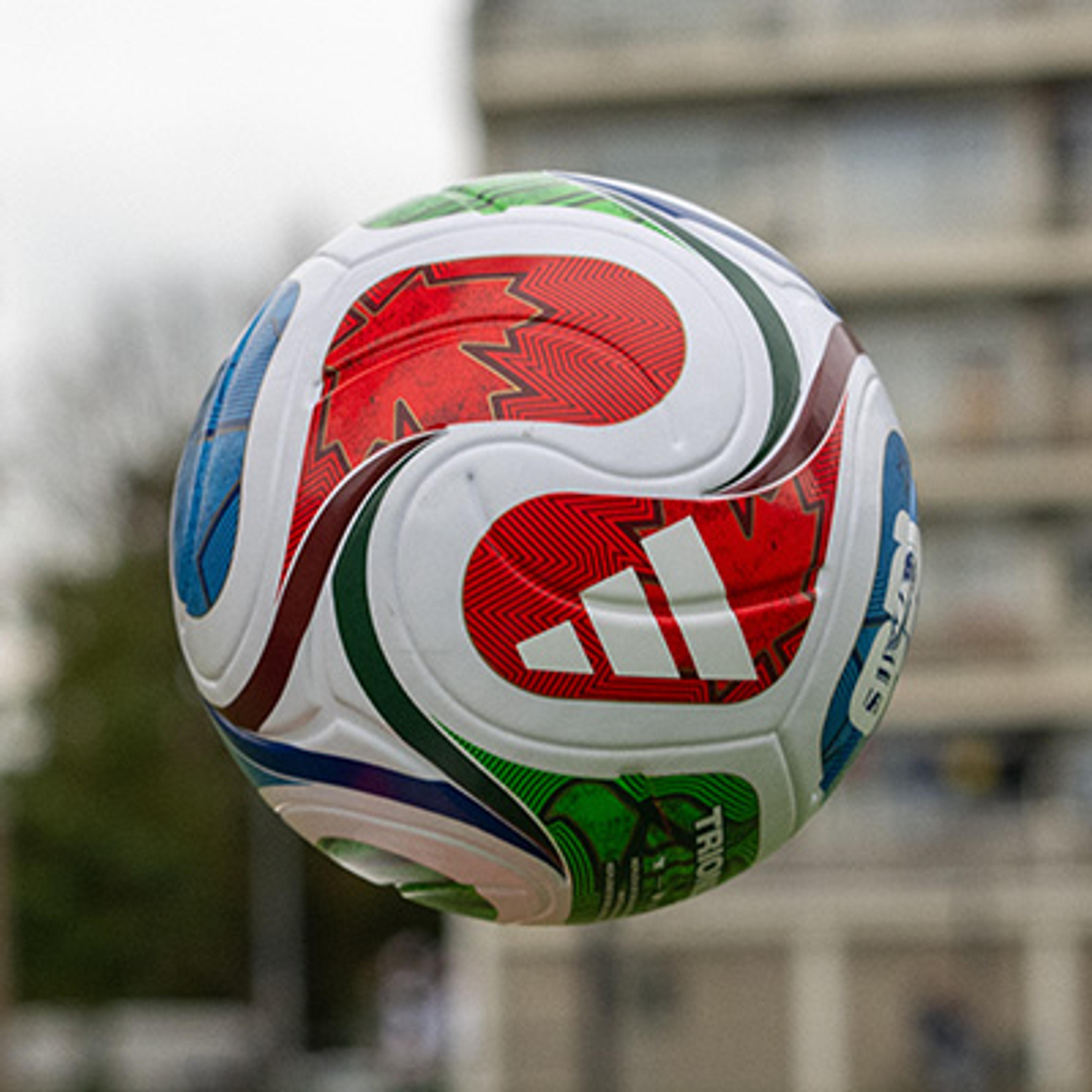 A white Adidas soccer ball with red, blue, and green patterns, floating in mid-air.