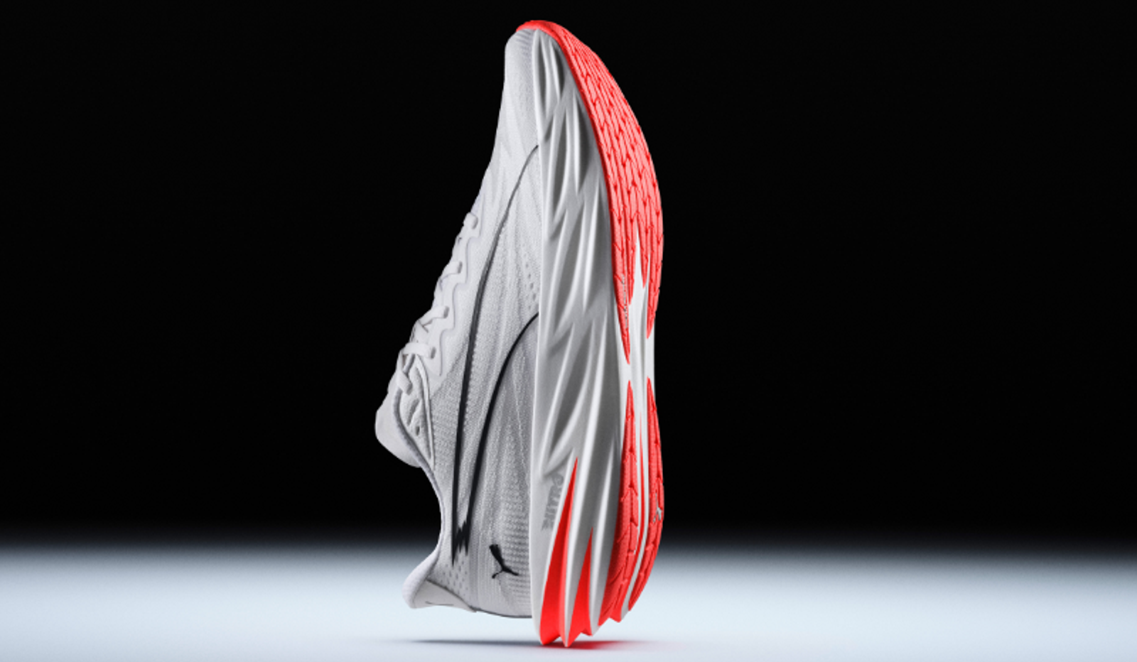 A white Puma running shoe with a bright coral-red sole, shown vertically against a dark background.