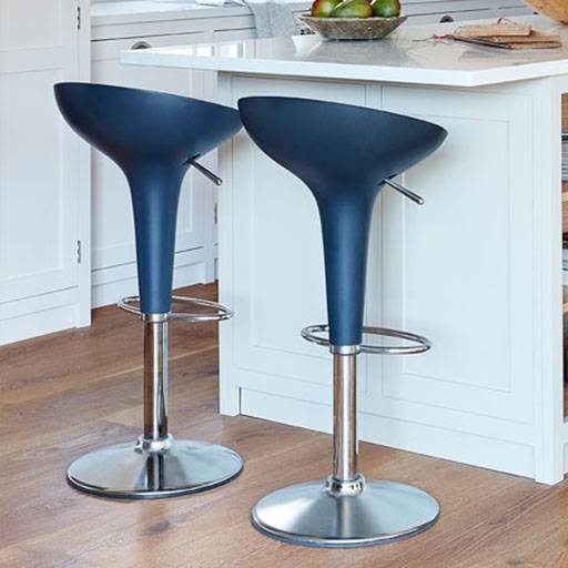 Two modern blue bar stools with chrome bases are placed next to a white kitchen island on a wooden floor. A bowl of green apples sits on the counter in the background.