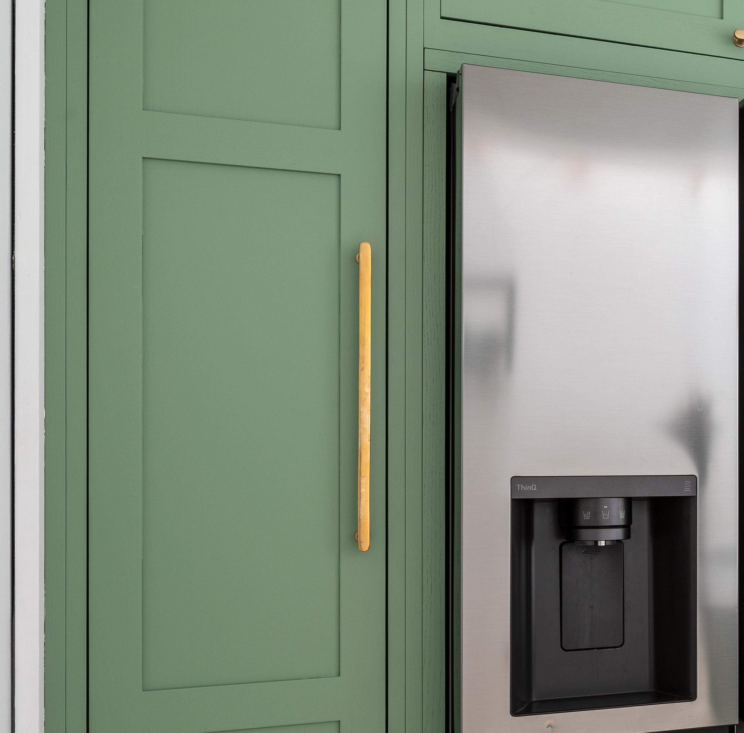 A stainless steel refrigerator with a built-in water and ice dispenser is next to a green cabinet with a long gold handle. The cabinet has a modern, flat-panel design.