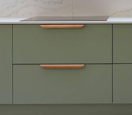 A close-up of sage green kitchen drawers with light wooden handles, set against a white countertop and a light marble-patterned backsplash.