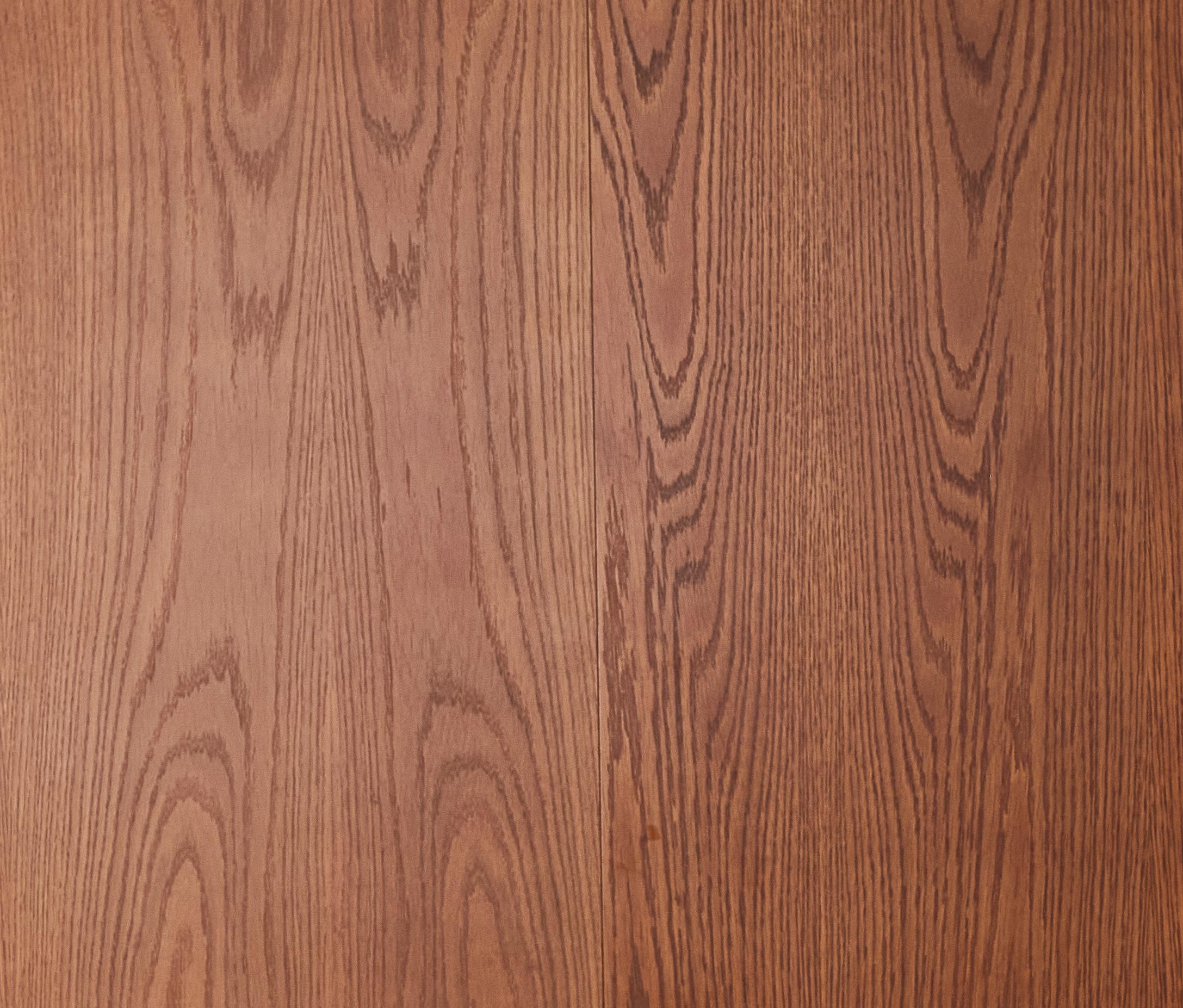 Wooden surface with a natural, light brown finish and visible grain patterns running vertically. The texture and color suggest a polished, traditional wood panel.