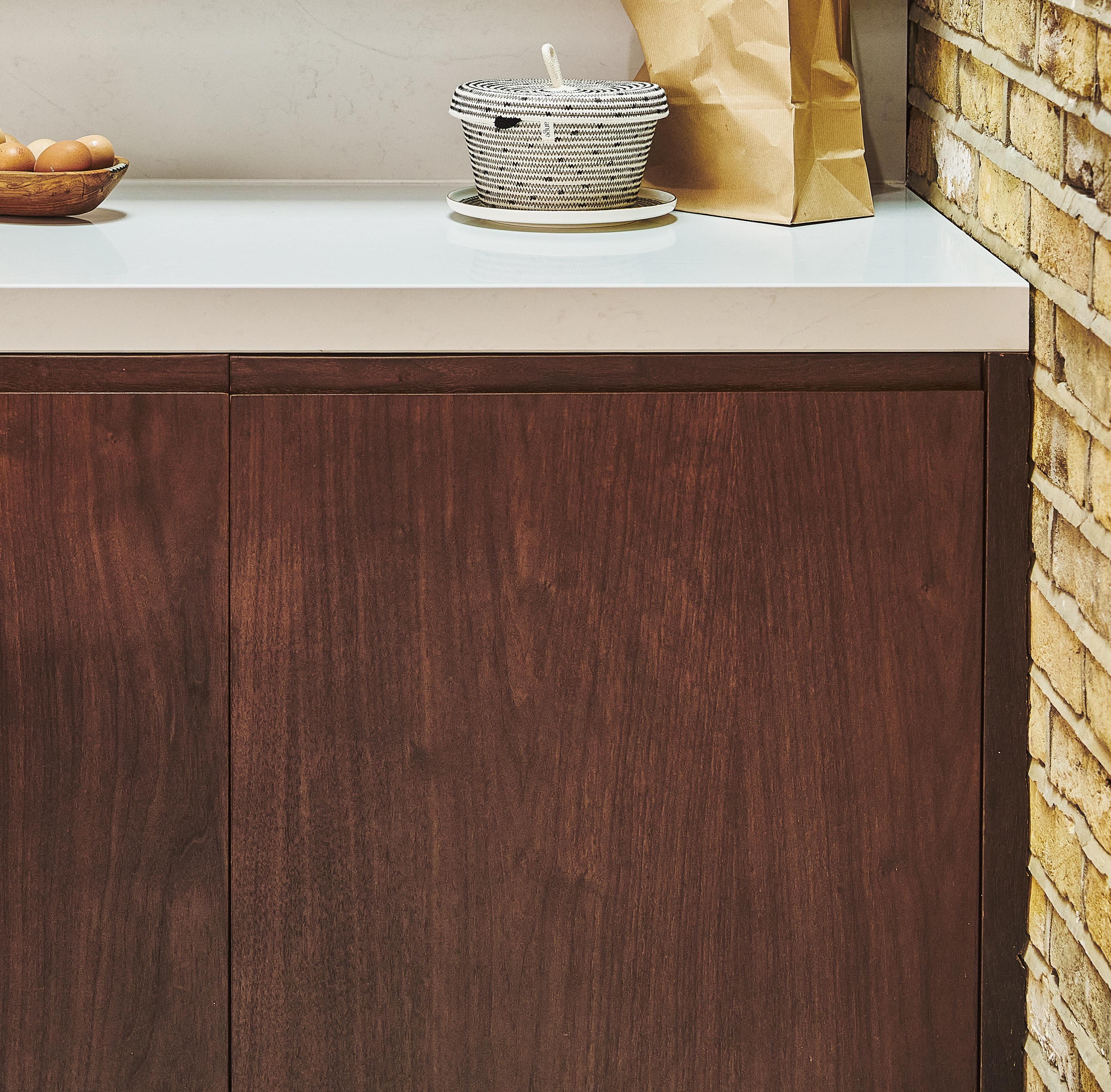 Close-up of a wooden cabinet with round cutout handles and a white marble countertop, set against a blurred dark background.