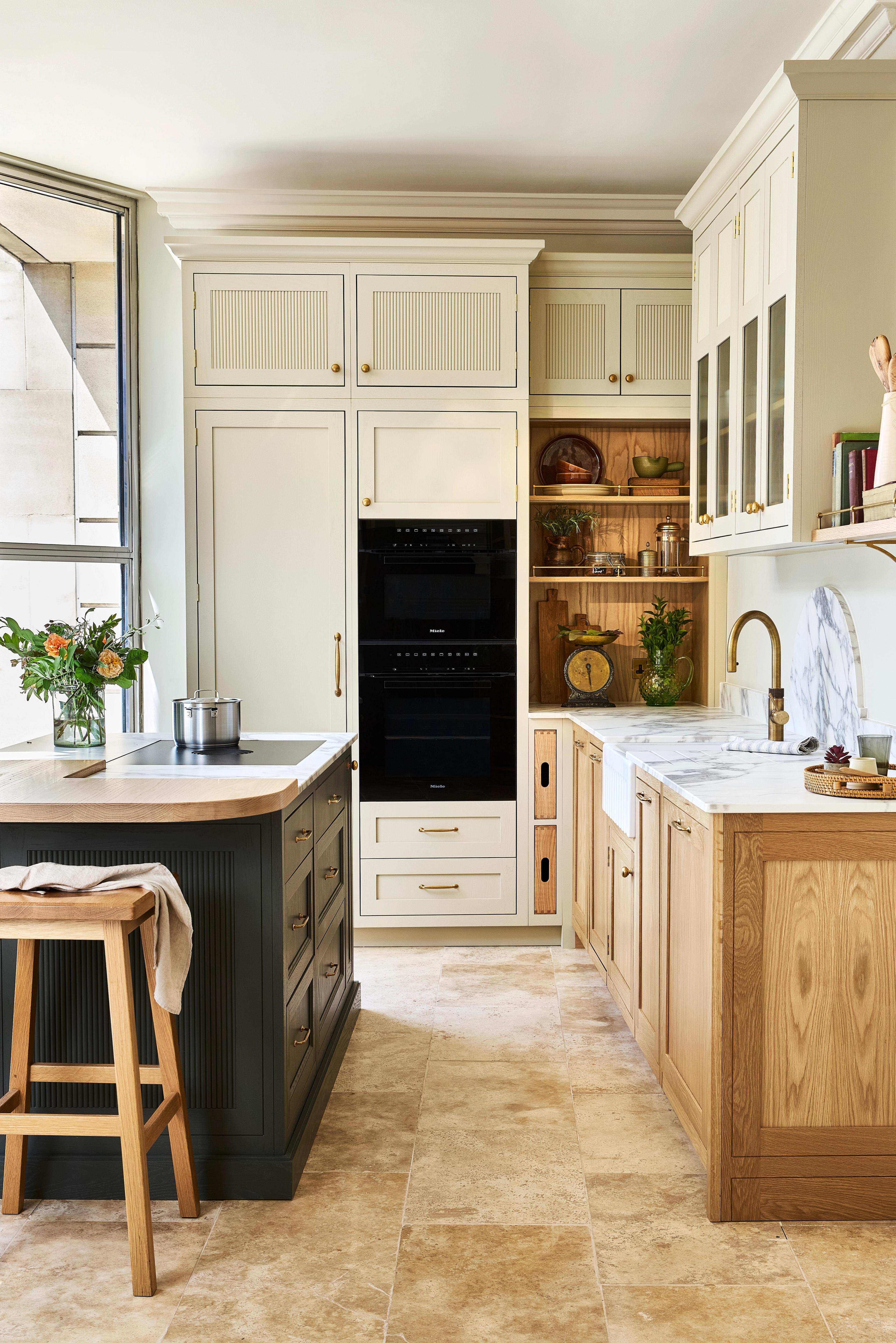 Bright, modern kitchen with pale blue cabinets, a farmhouse sink, white walls, open shelves holding dishes and plants, a window with a sheer white blind, and a dark herringbone-patterned floor.