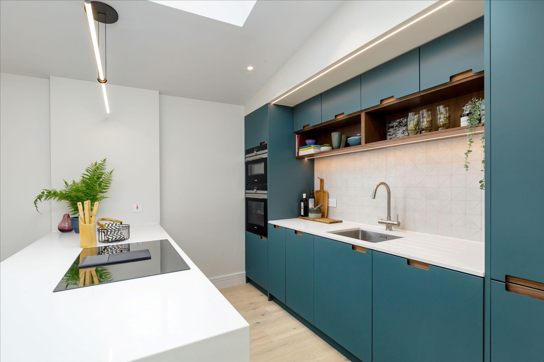 A bright kitchen with a large window, blue cabinets with glass doors, and a marble-topped island. Two wooden bar stools sit by the island, and a vase of pink roses is on the counter. A pendant light hangs above.