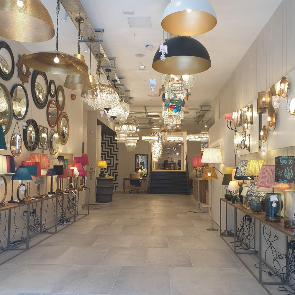 A spacious lighting store showroom filled with an extensive collection of hanging chandeliers, modern pendant lights, wall sconces, and colorful table lamps displayed on side tables.