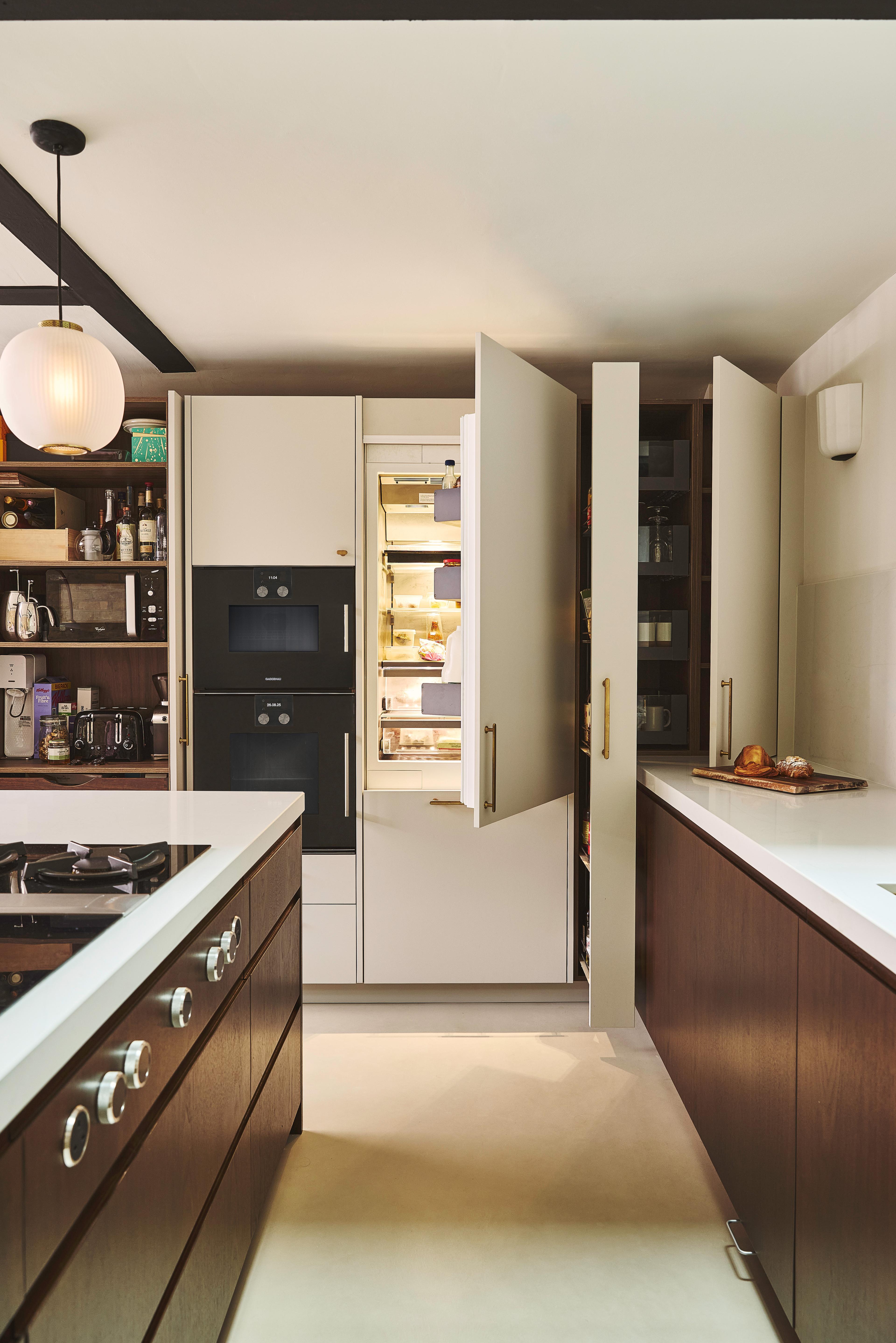 Modern kitchen with cream-colored cabinets, gold handles, dark wood lower cabinets, built-in black oven, white countertops, and a round hanging light fixture. A loaf of bread sits on the counter.