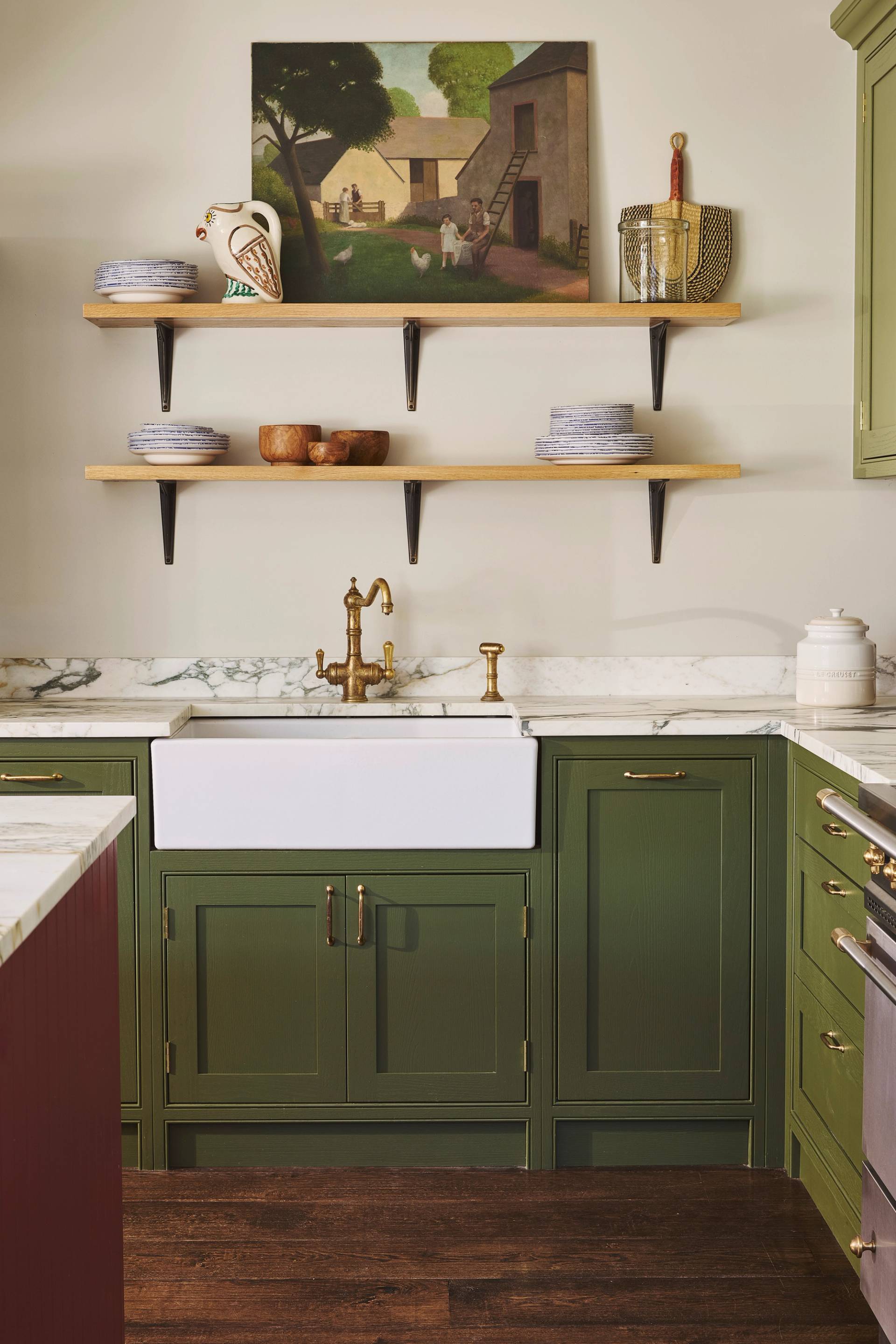 Modern kitchen with cream-colored cabinets, gold handles, dark wood lower cabinets, built-in black oven, white countertops, and a round hanging light fixture. A loaf of bread sits on the counter.
