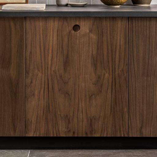 A close-up of a wooden cabinet with three doors, featuring a round finger hole on the center door, set below a gray countertop and decorative items.