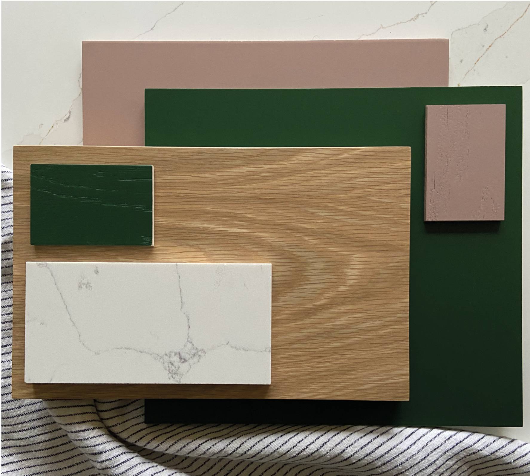 A flat lay of materials including large and small green and pink tiles, a wooden panel, a white marble-look piece, and a striped fabric at the bottom, displaying a collection of textures and colors.