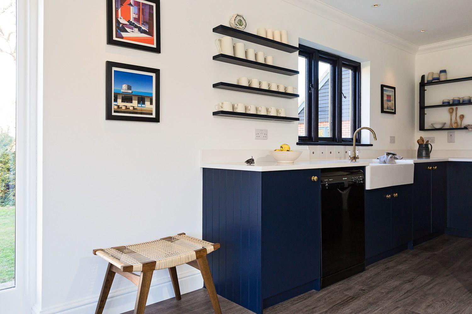 Custom blue paint sets a bold & elegant statement in this sleek modern kitchen, complemented by dark wooden floors & black shelves.