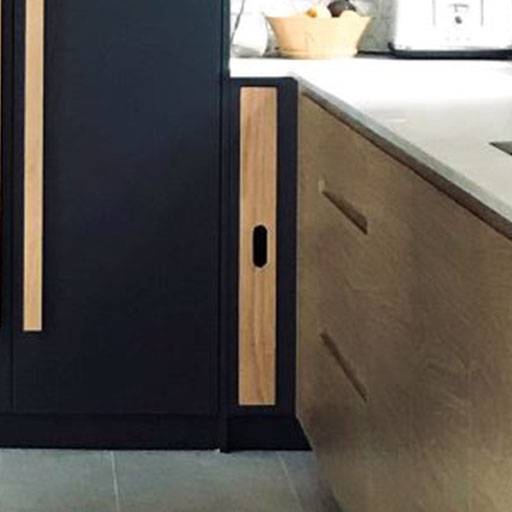 A small, narrow cabinet with a wood finish is built into a kitchen, positioned between a tall black cabinet and a light wood counter with drawers.