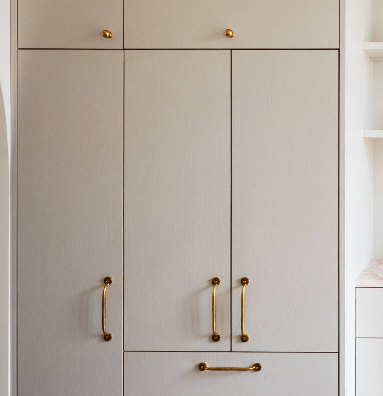 A close-up of a beige-colored cabinet with gold handles, featuring upper, middle, and lower compartments, set against a light background.