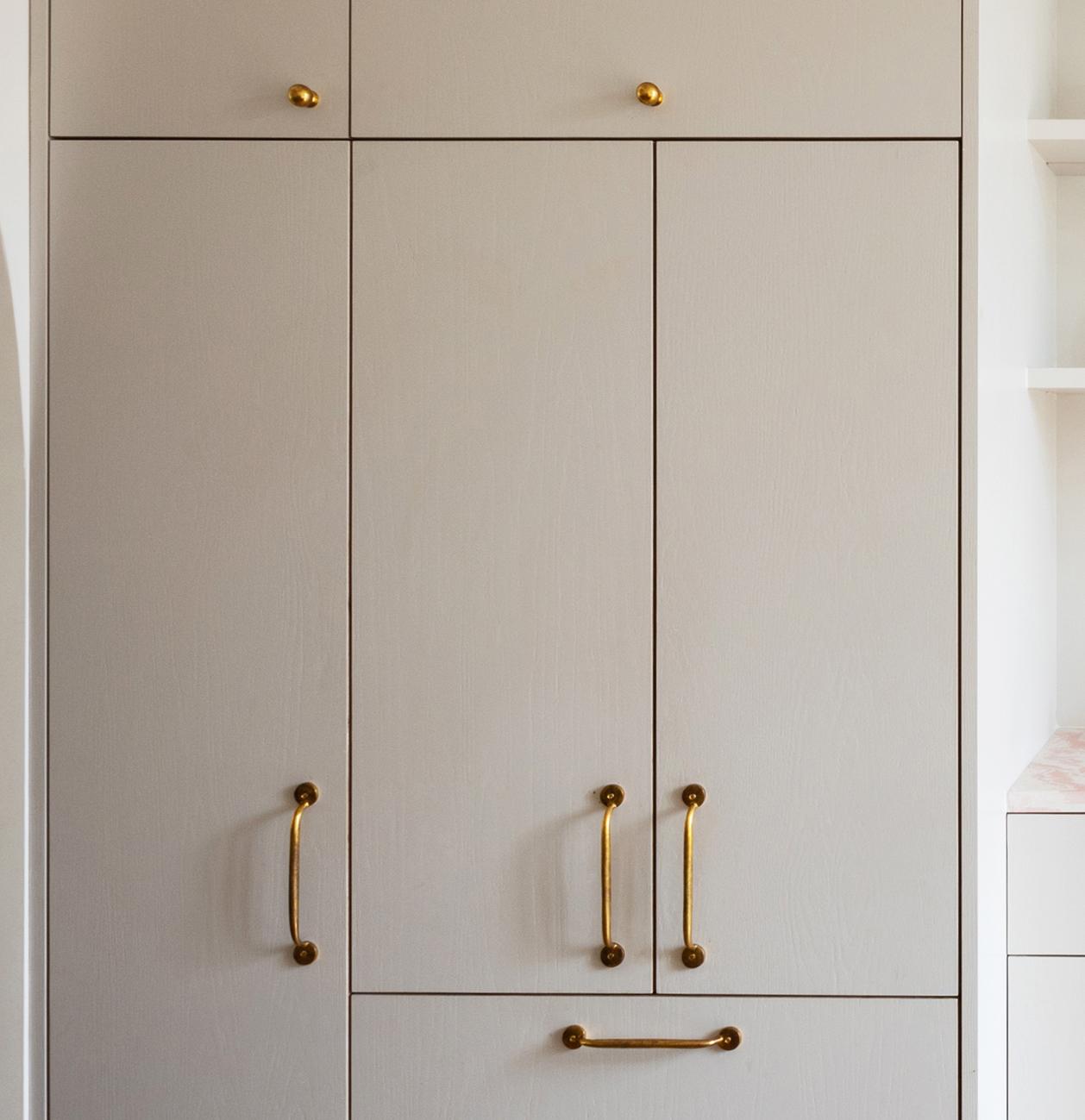 A close-up of a beige-colored cabinet with gold handles, featuring upper, middle, and lower compartments, set against a light background.