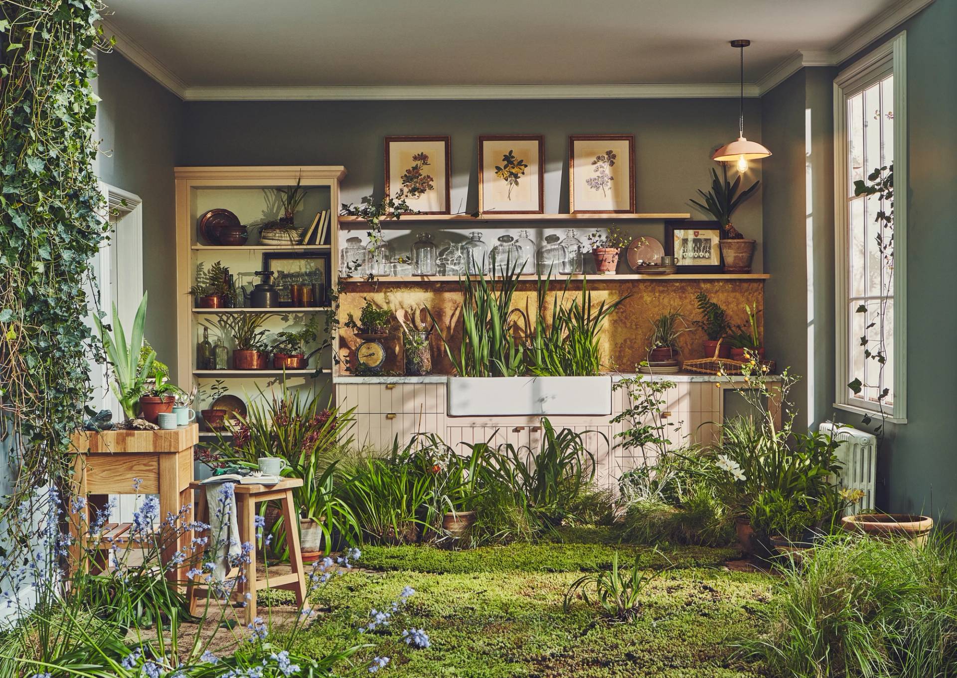 Bespoke wooden kitchen overgrown with a lush indoor forest, featuring a moss-covered floor, tall grasses in a butler sink, and climbing ivy. Professional kitchen design integrated with a wild, botanical conservatory aesthetic.