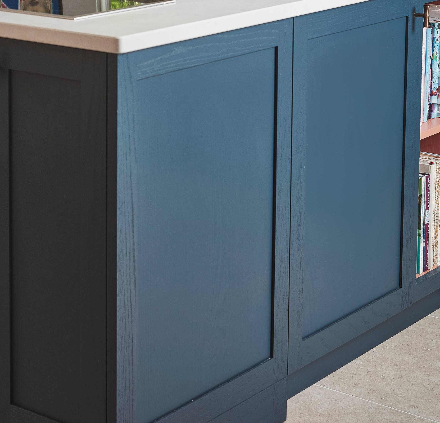 Blue kitchen island with a white countertop and integrated bookshelf on the side, partially visible with books neatly arranged on the lower shelf.