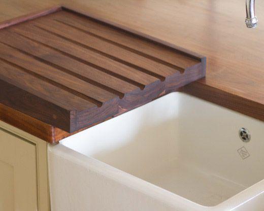 A kitchen sink with white ceramic basin is partially covered by a wooden cutting board with grooves. The board rests on a wooden countertop, integrating seamlessly with the kitchen design. A silver faucet is visible in the upper right corner.