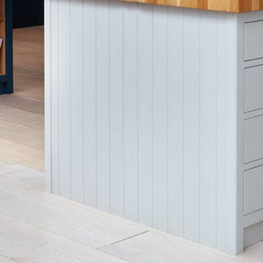 Light gray vertical paneling on the side of a kitchen island with a wooden countertop and light-colored tiled floor. Drawers are visible on the right side.