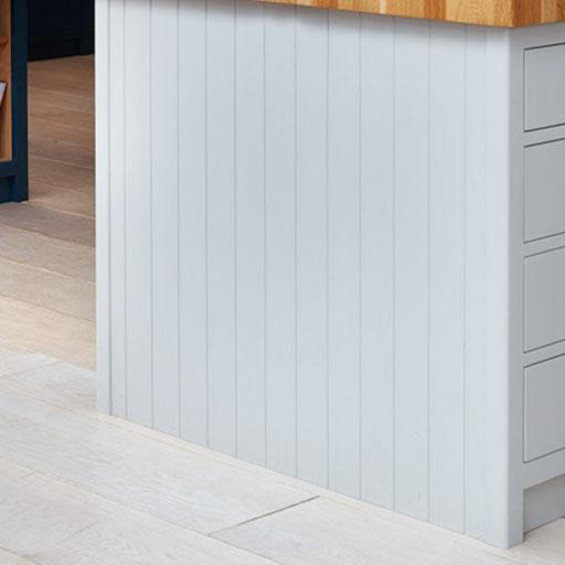 Light gray vertical paneling on the side of a kitchen island with a wooden countertop and light-colored tiled floor. Drawers are visible on the right side.