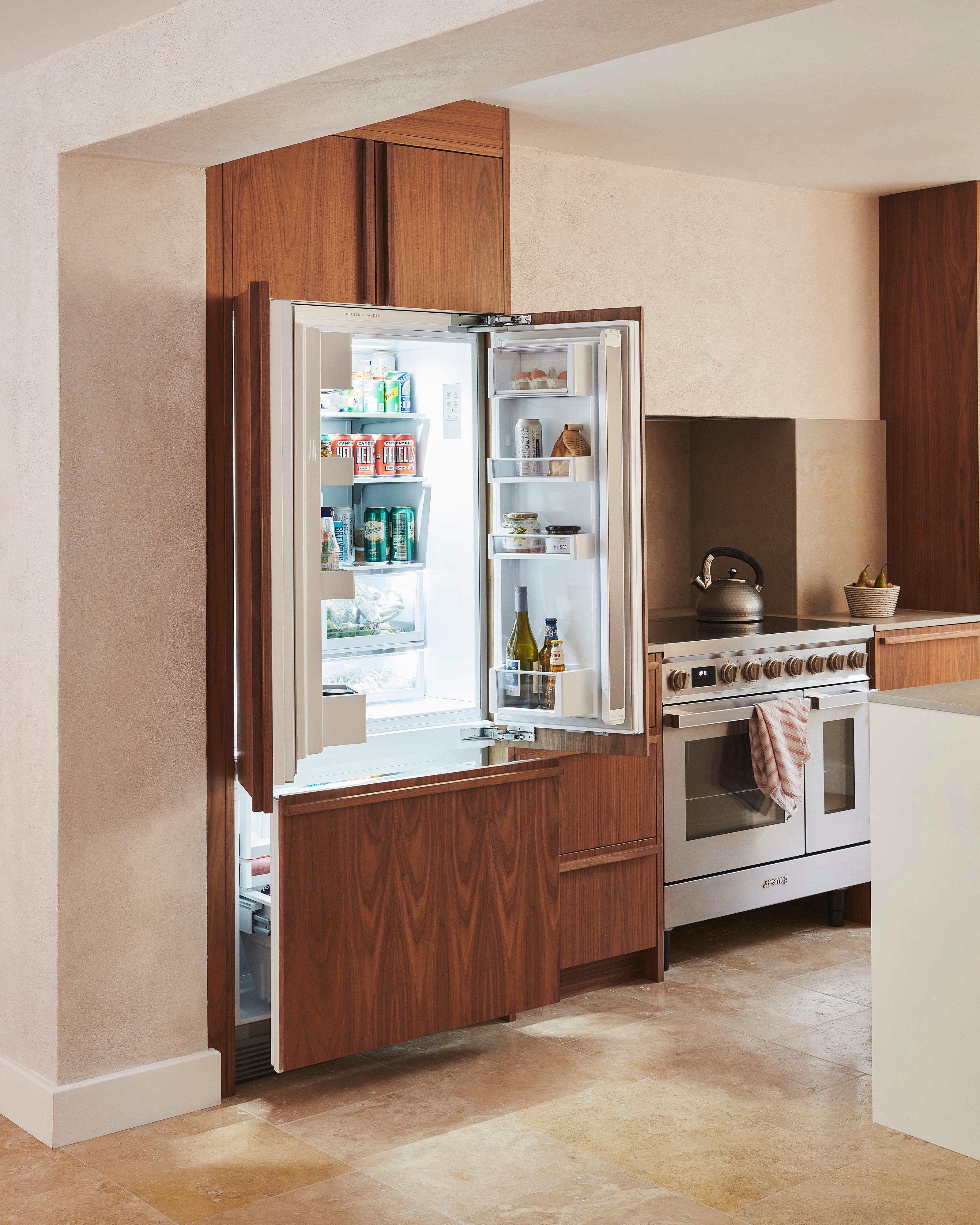 A modern kitchen with wooden cabinets, a stainless steel oven, and a white countertop. A kettle sits on the stovetop, and a small plant is placed on the counter next to the oven. The floor is made of light beige tiles.