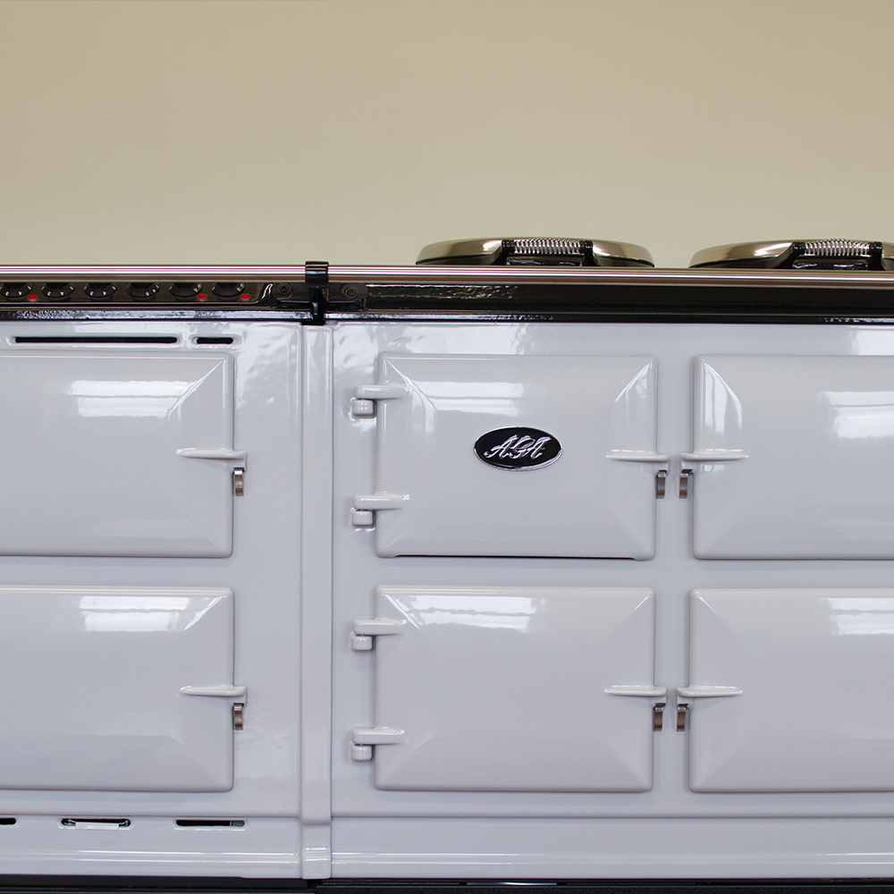 Close-up of a classic white AGA cooker with multiple oven doors and two metal hob covers on top, set against a plain beige background.