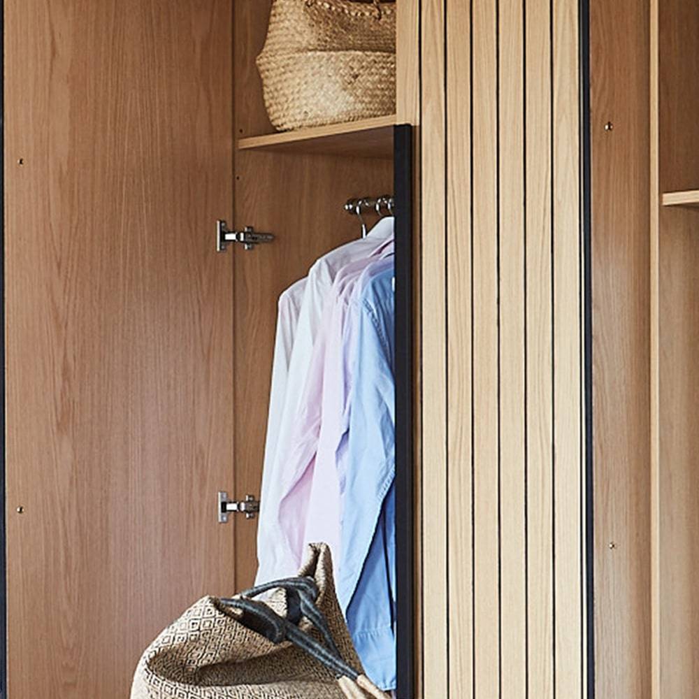 An open wooden wardrobe displaying two shirts hanging inside, with woven baskets placed on the shelves above and below.