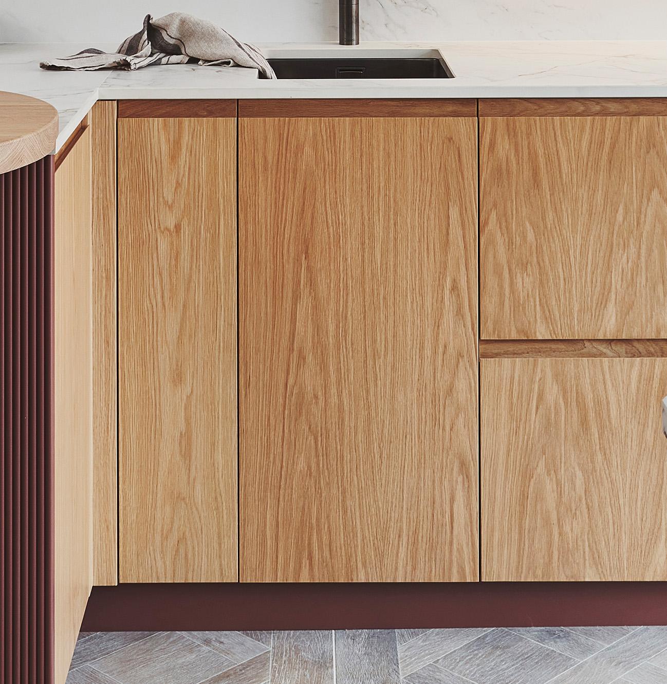 Modern kitchen with light wood cabinets and marble countertops. A kitchen towel is placed near the sink. The flooring has a geometric pattern in neutral tones.