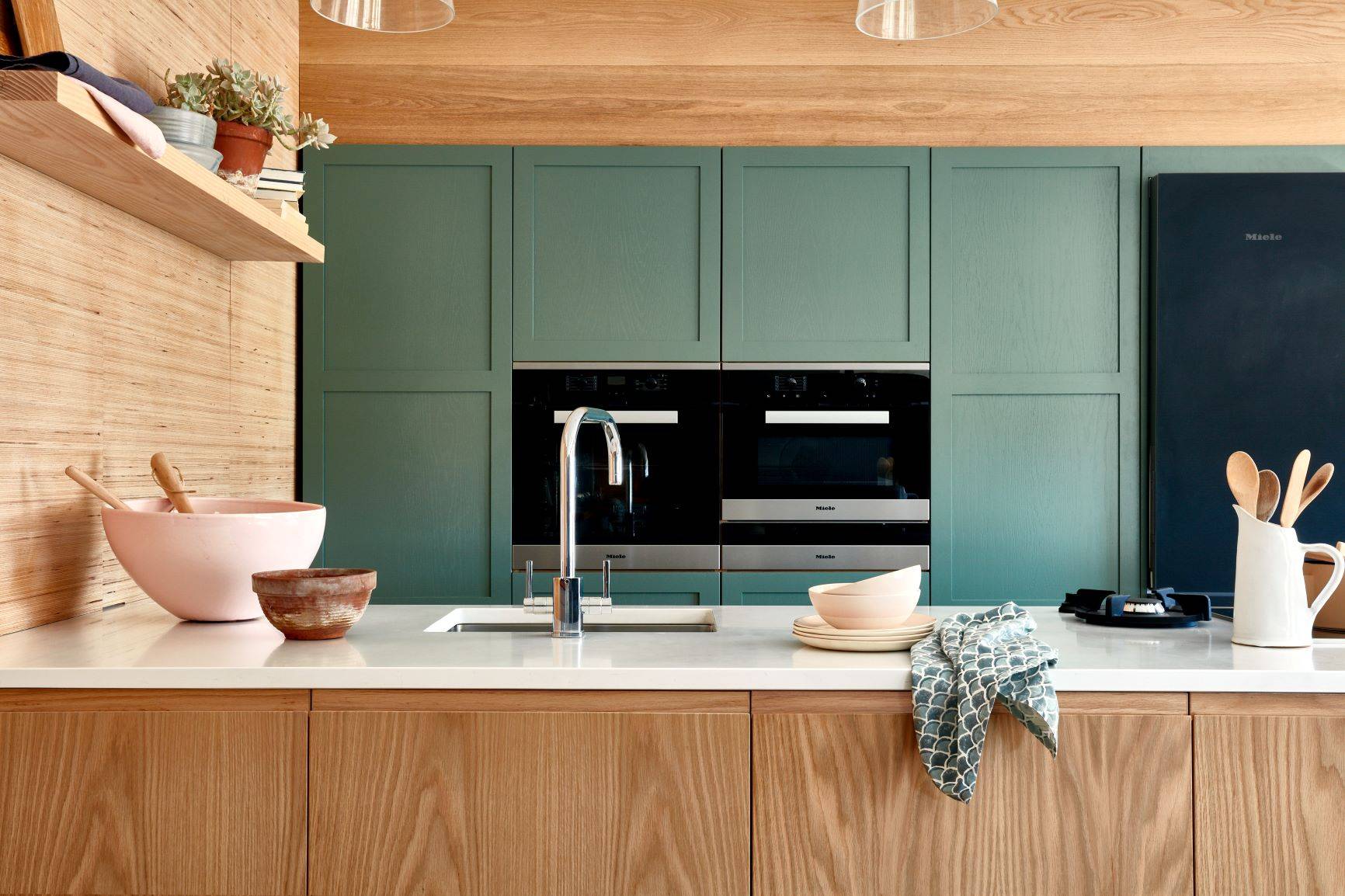 Oak base cabinets with green tall cabinets. bowls and wooden spoons on white marble worktop