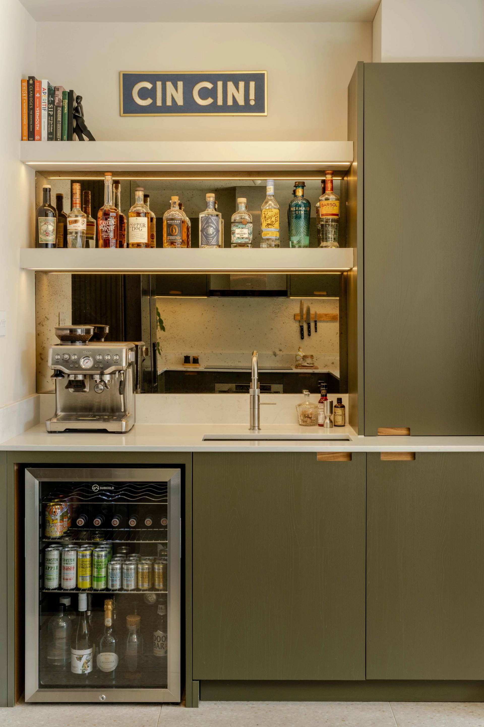 Modern kitchen with burgundy and wood tones. Open shelves display books, plates, and decorative birds. Marble backsplash and countertop enhance the design. A green plant hangs over the counter, and there are towels next to the stove area