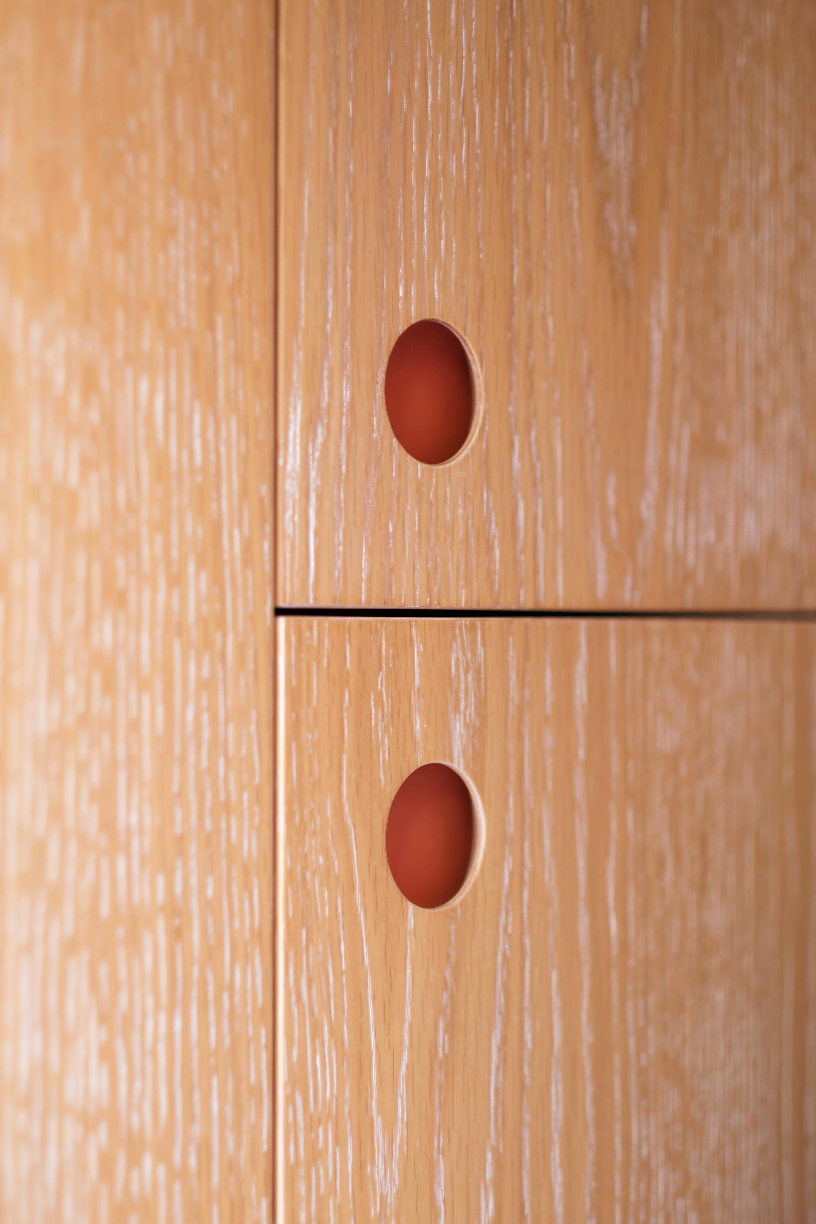 Close-up of two light wood cabinet doors with round, recessed reddish-brown handles, showing the wood grain texture and minimalist design.