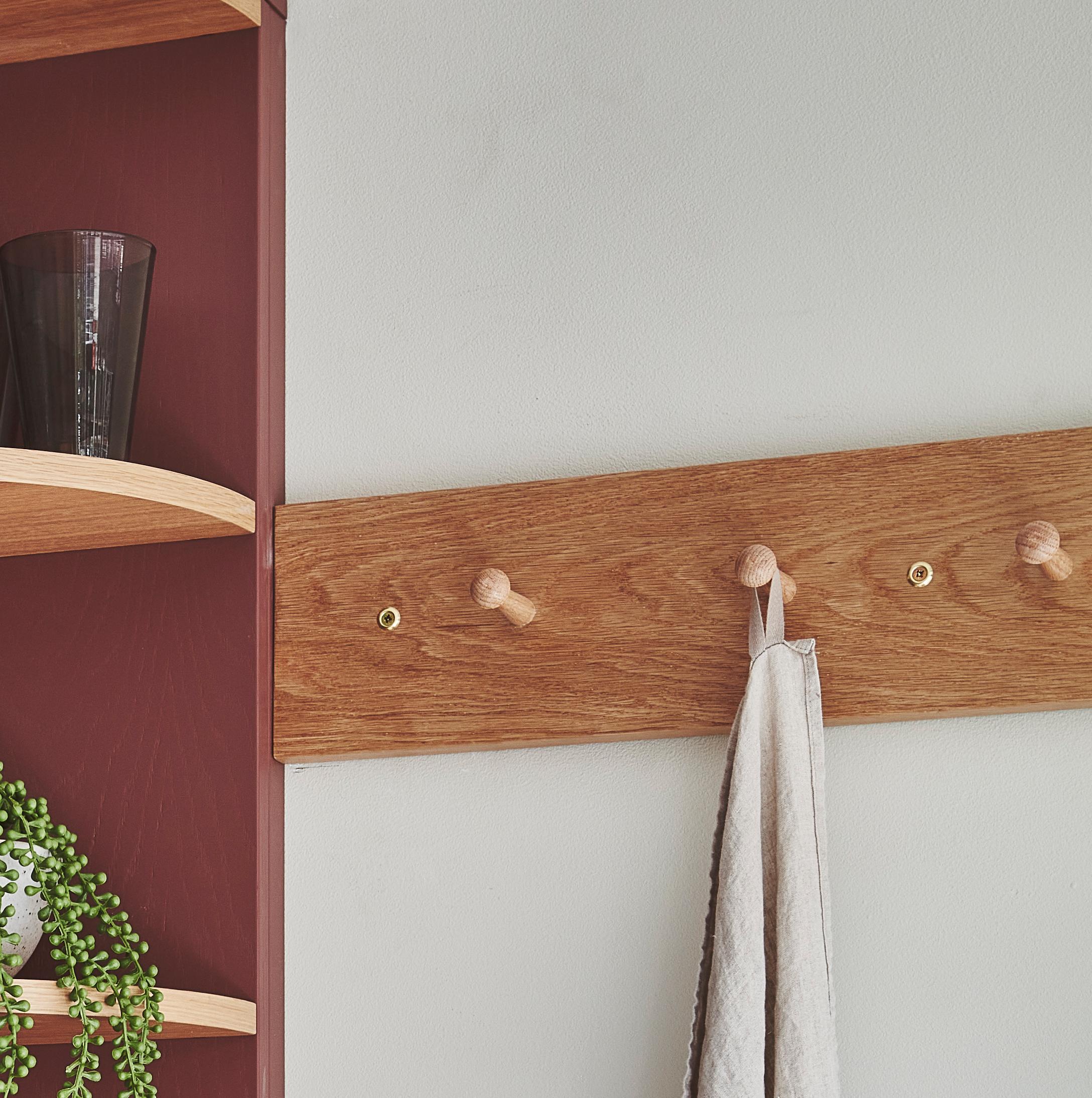 Wooden pegboard with a hanging towel is mounted on a white wall next to a burgundy wall with corner shelves. A glass and a potted plant are on the shelves