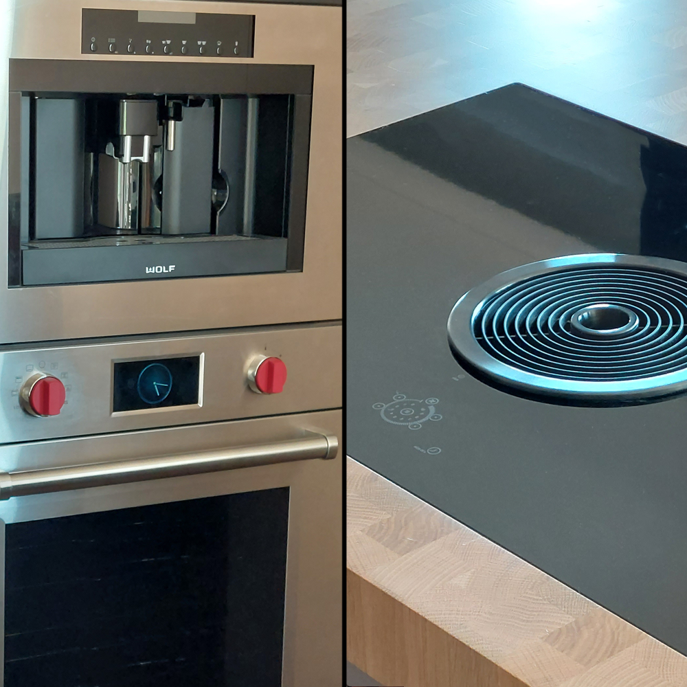 A modern kitchen shows a built-in stainless steel coffee machine and oven with red knobs on the left, and a sleek black induction cooktop with a central vent on a wooden counter on the right.