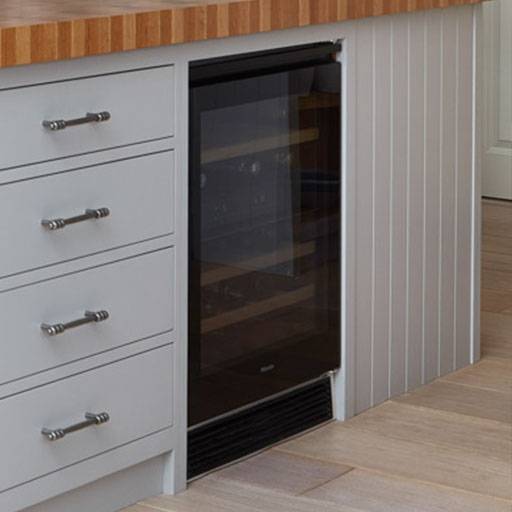 A built-in wine cooler with a glass door is installed under a wooden countertop next to gray drawers with silver handles in a modern kitchen.